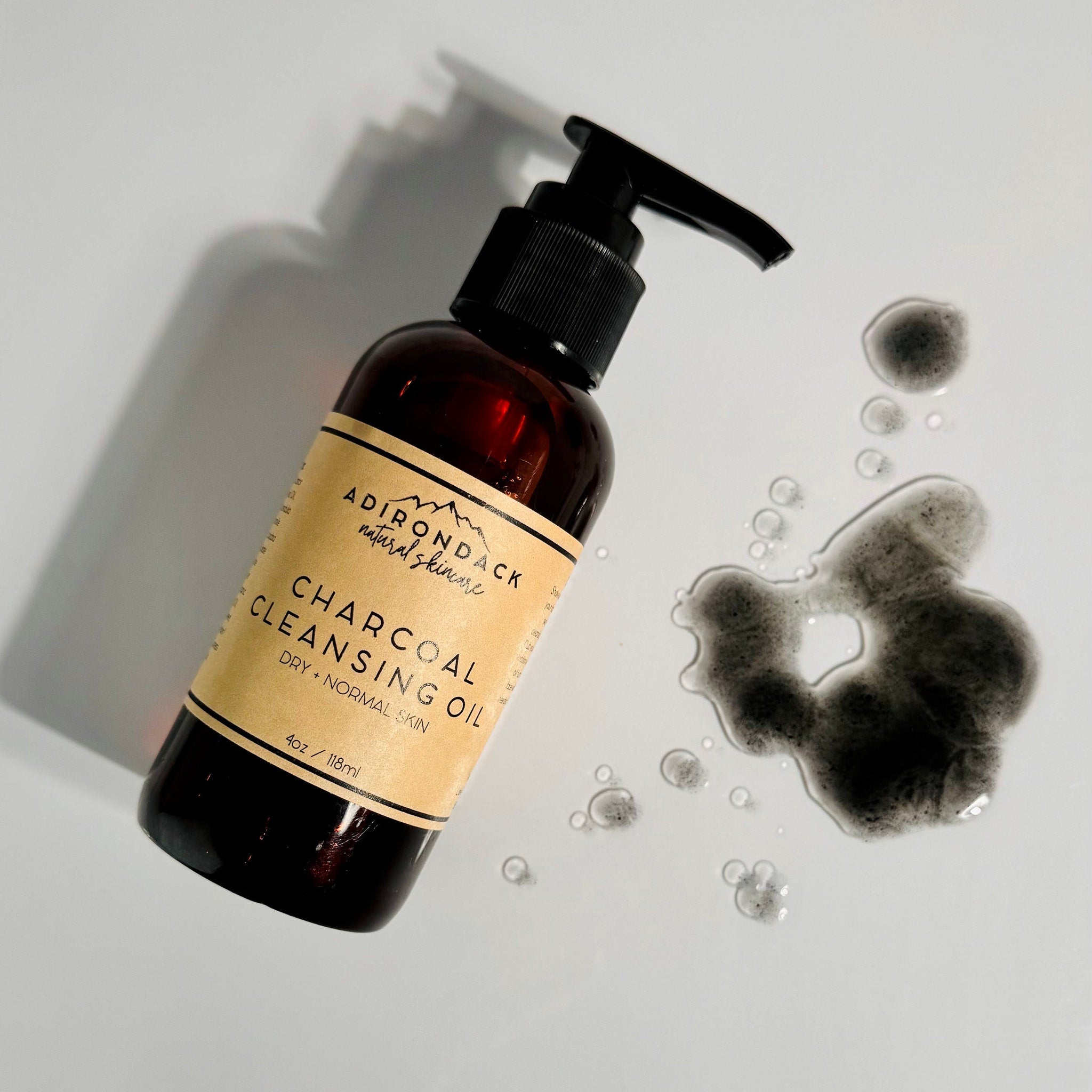 Charcoal cleansing oil bottle with brown glass, black pump, and charcoal residue