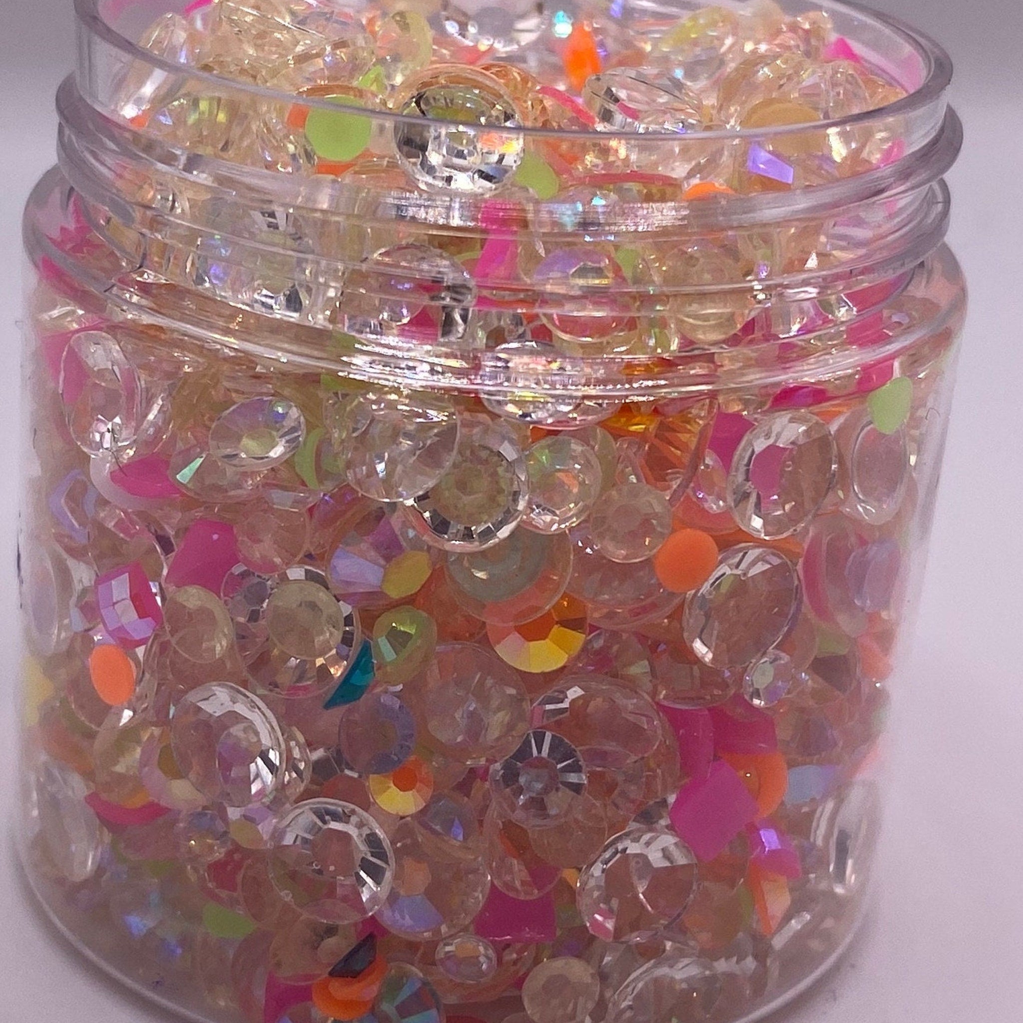 Rhinestone mix with clear, pink, and orange accents inside a clear jar for crafts