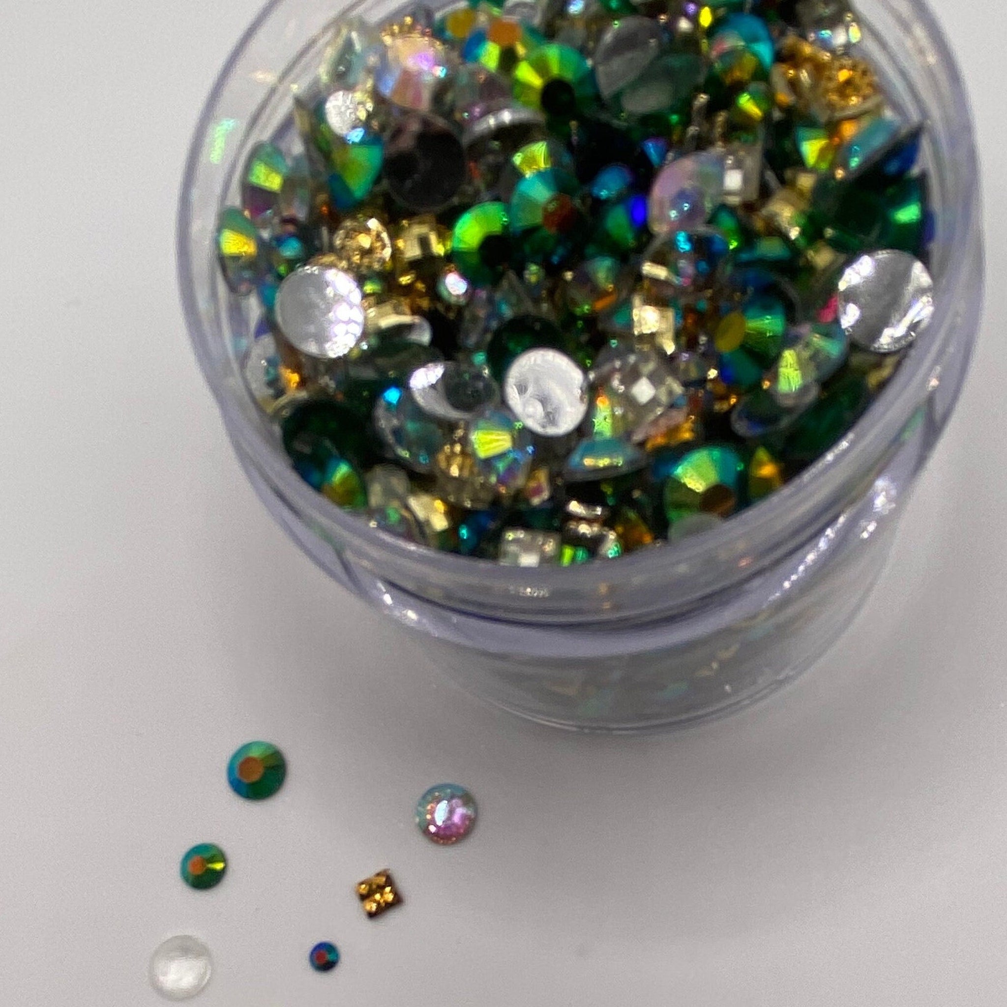 Rhinestones in clear container with green, gold, and silver iridescent colors, small round and square shapes
