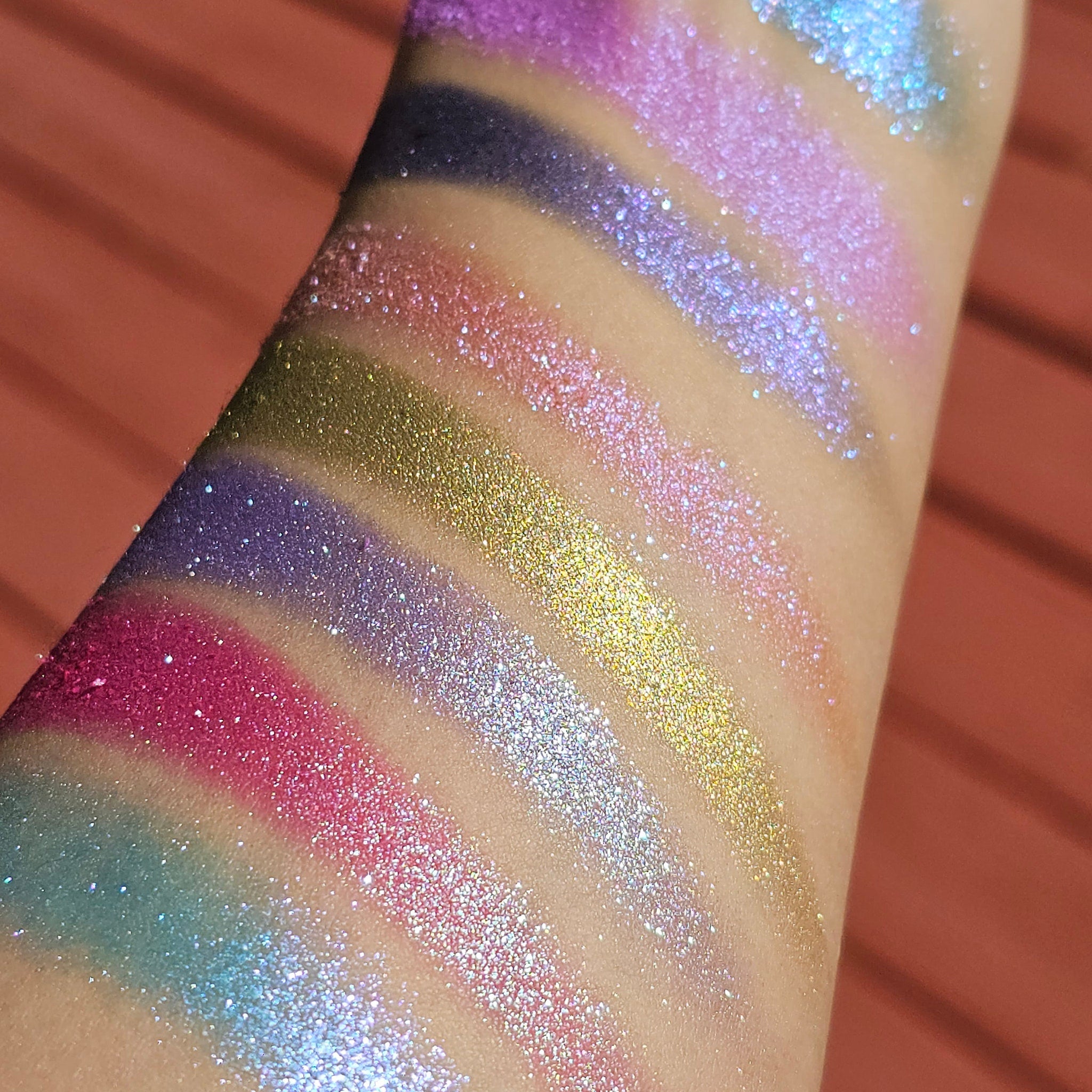 Eyeshadow swatches with various colors including pink, purple, blue, and gold, applied on skin for color display