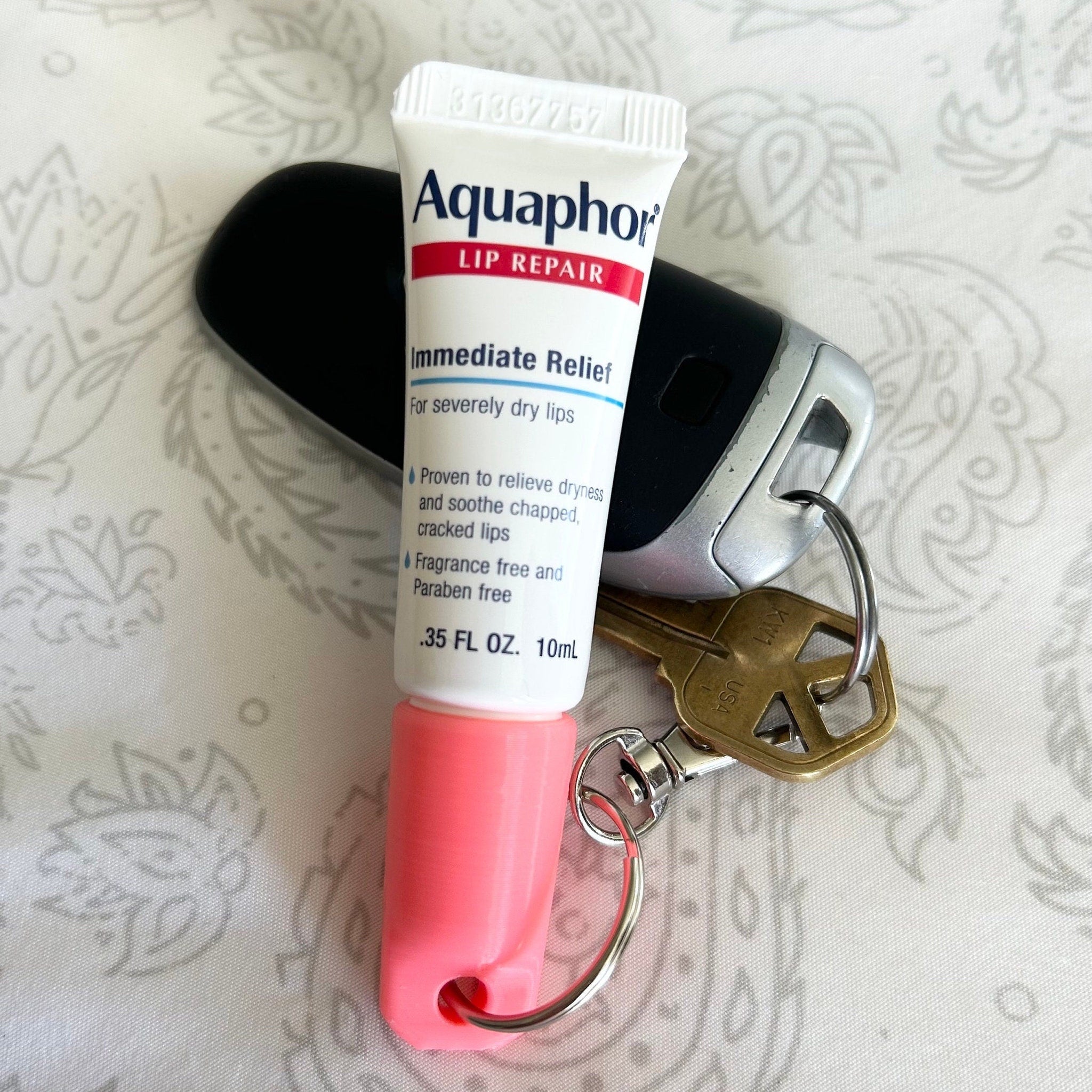 Aquaphor lip repair tube, white and red tube with pink holder, next to car key