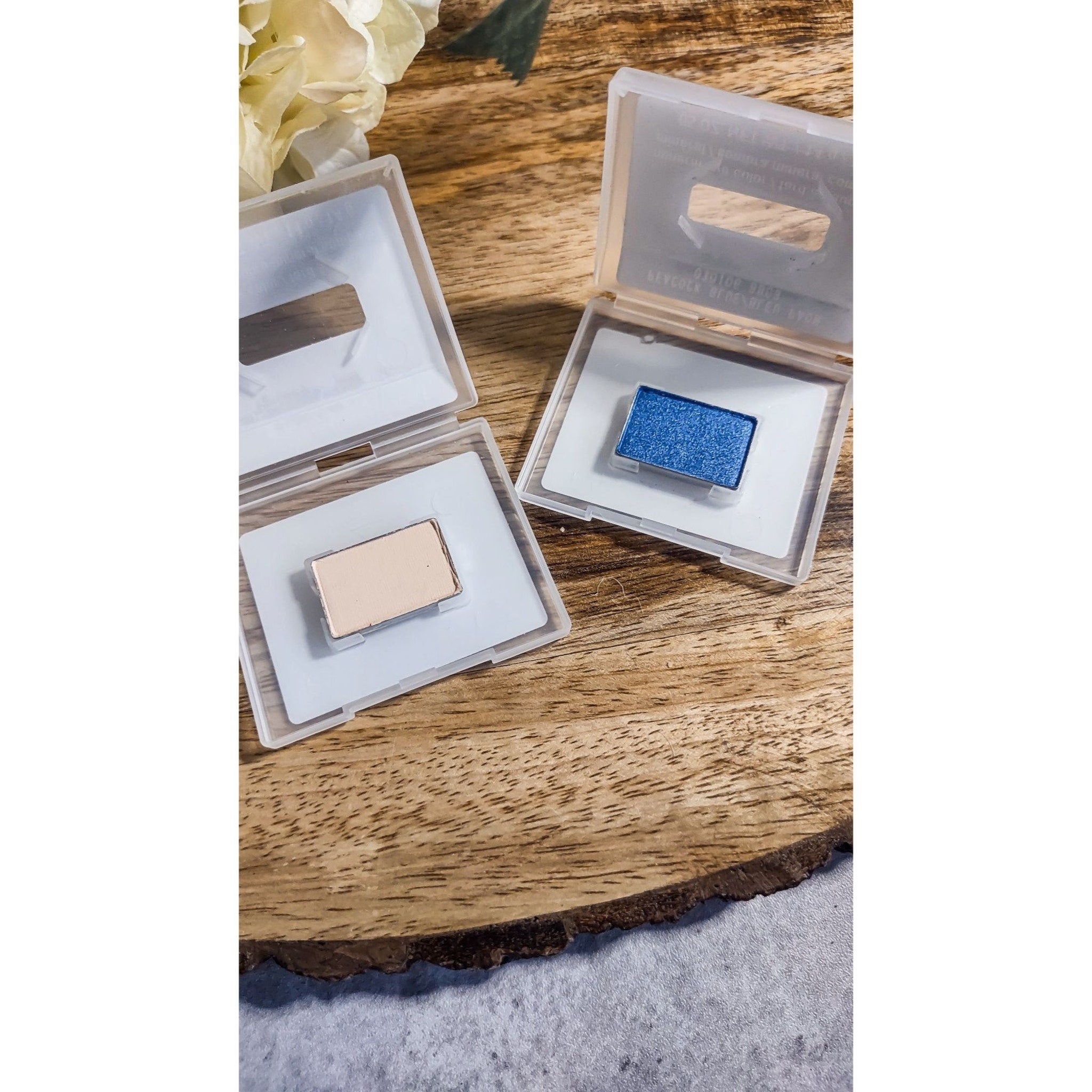 Eyeshadow compacts with blue and beige shades in clear plastic cases on wood surface
