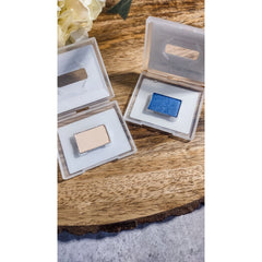 Eyeshadow compacts with blue and beige shades in clear plastic cases on wood surface