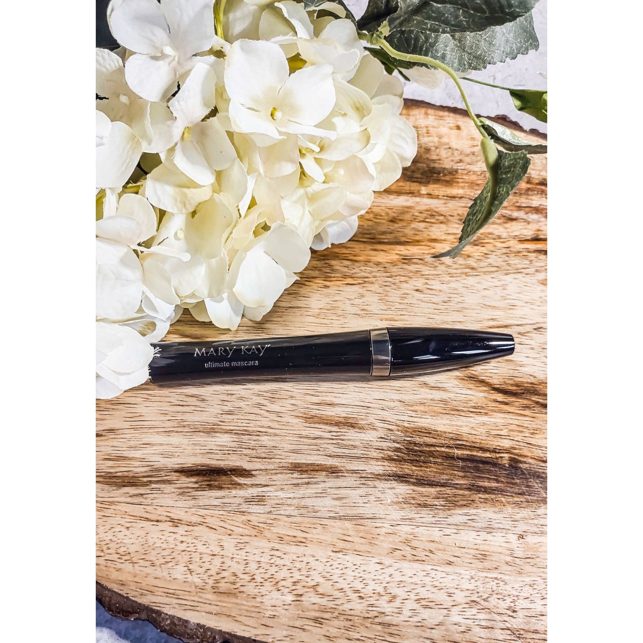 Mascara tube, black with silver band, Mary Kay brand on wooden surface with flowers