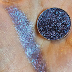 Eyeshadow compact with blue and purple shimmer, swatched on skin, round metal pan