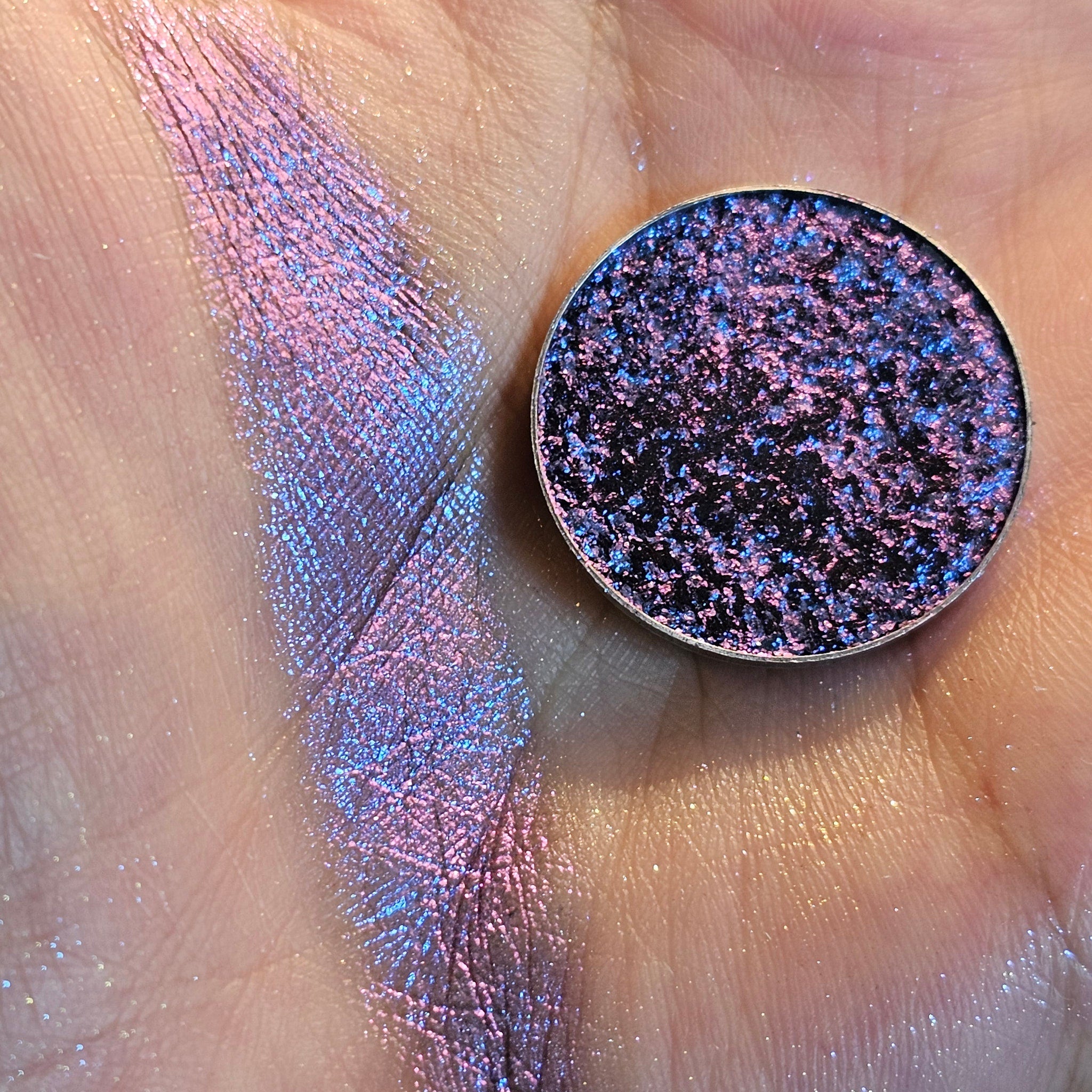 Eyeshadow swatch with pink, blue, and purple shimmer on skin, round compact shown