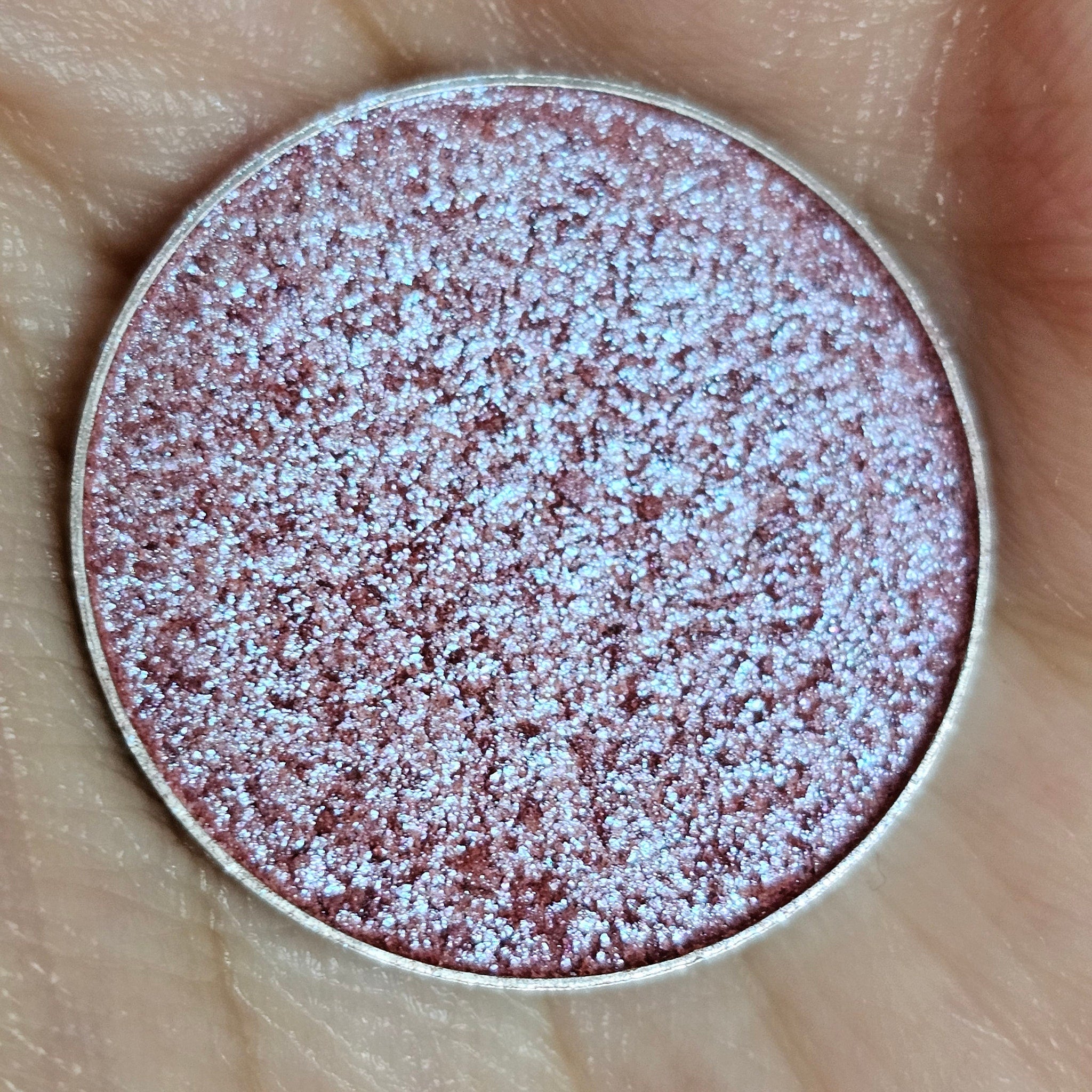Eyeshadow compact with iridescent pink and blue shimmer, metallic silver rim, held in hand