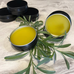 Yellow balm in black metal tins with green leaves on a marble surface