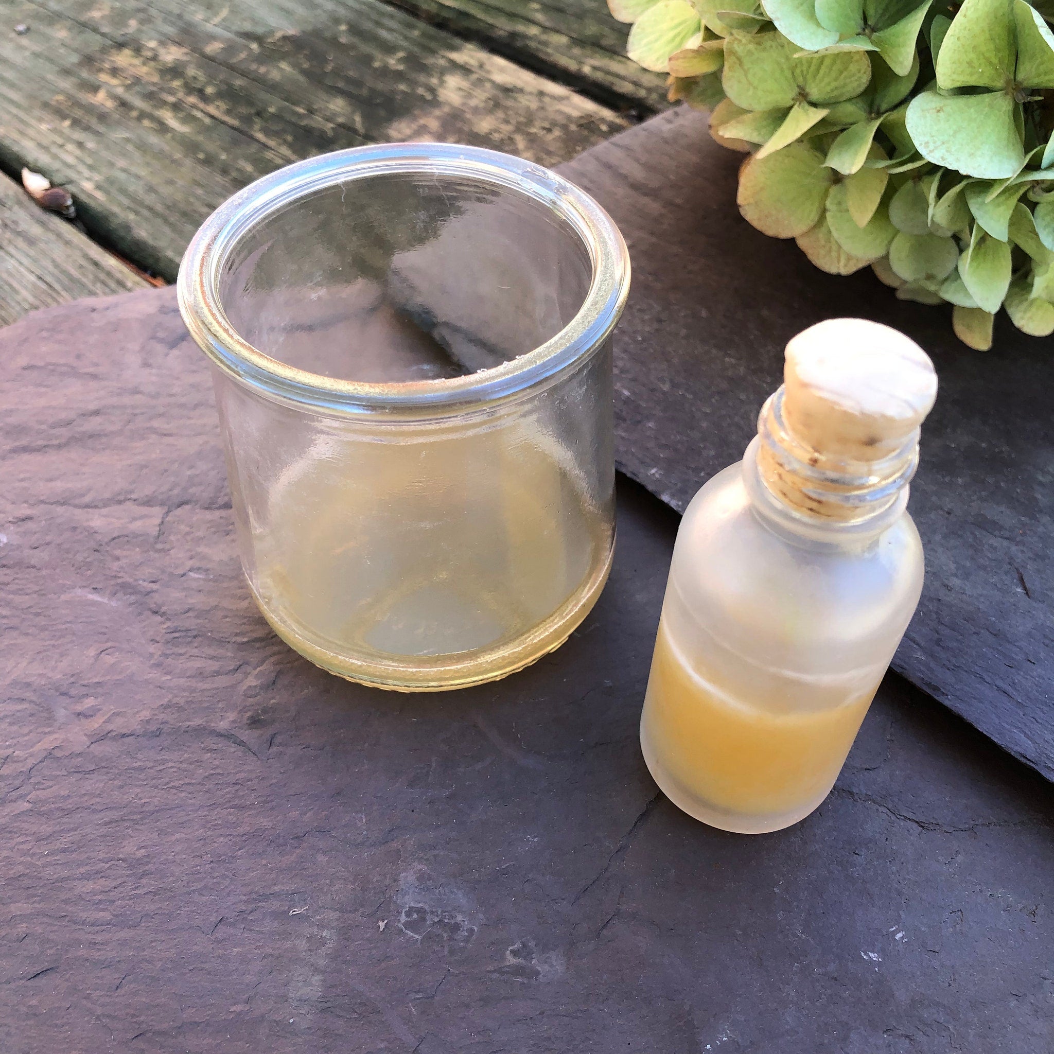 Glass jar with yellow liquid, small glass bottle with cork, on dark stone surface.