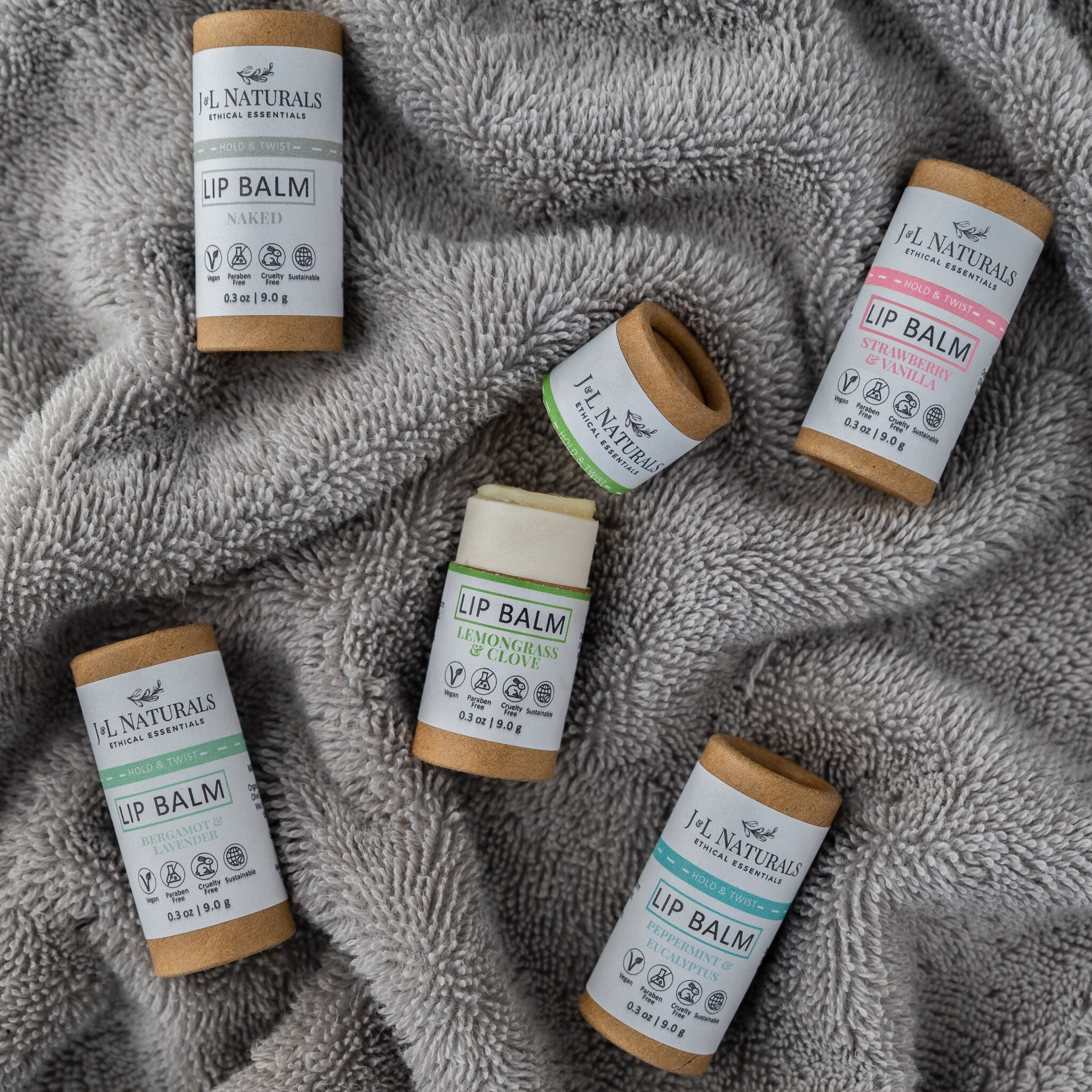 Lip balm tubes with brown cardboard, white labels, and JNL Naturals branding on gray fabric