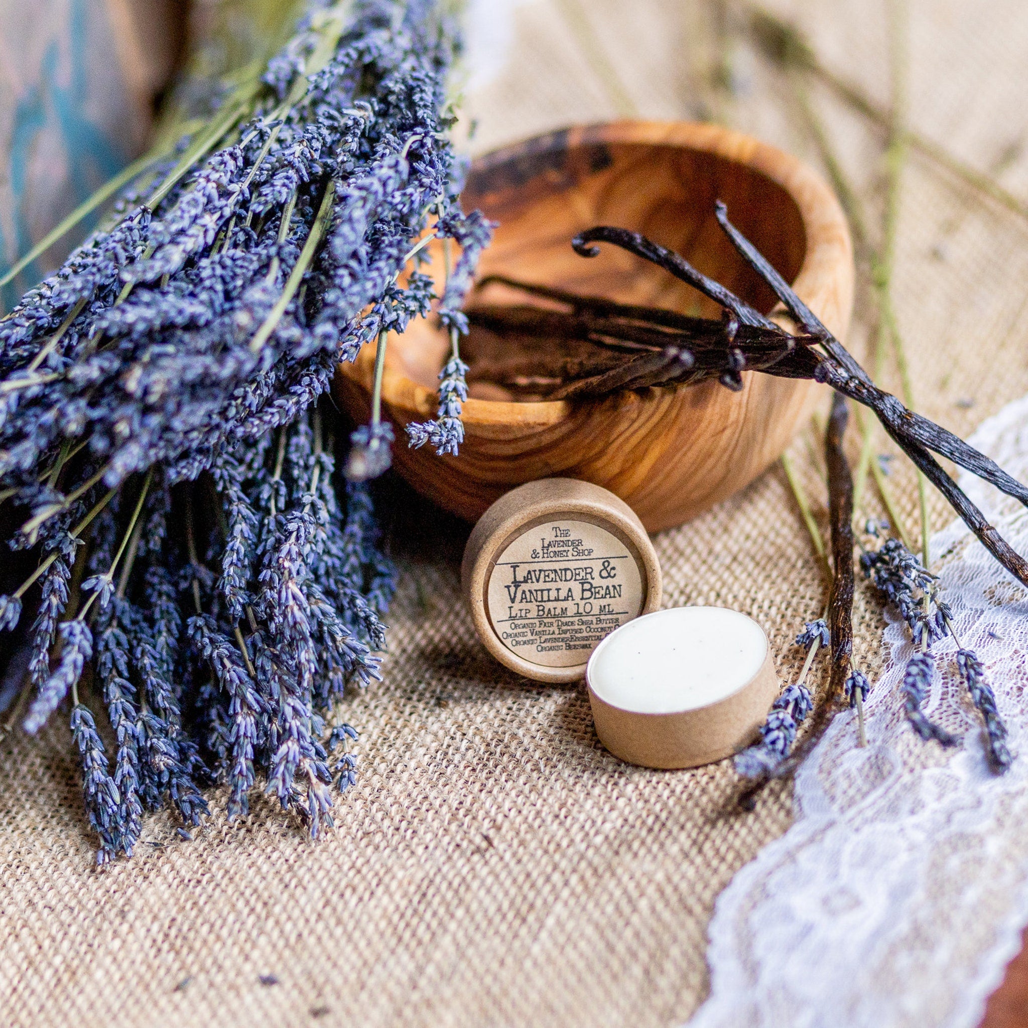 Lip balm with white cream, brown paper container, lavender and vanilla bean arrangement