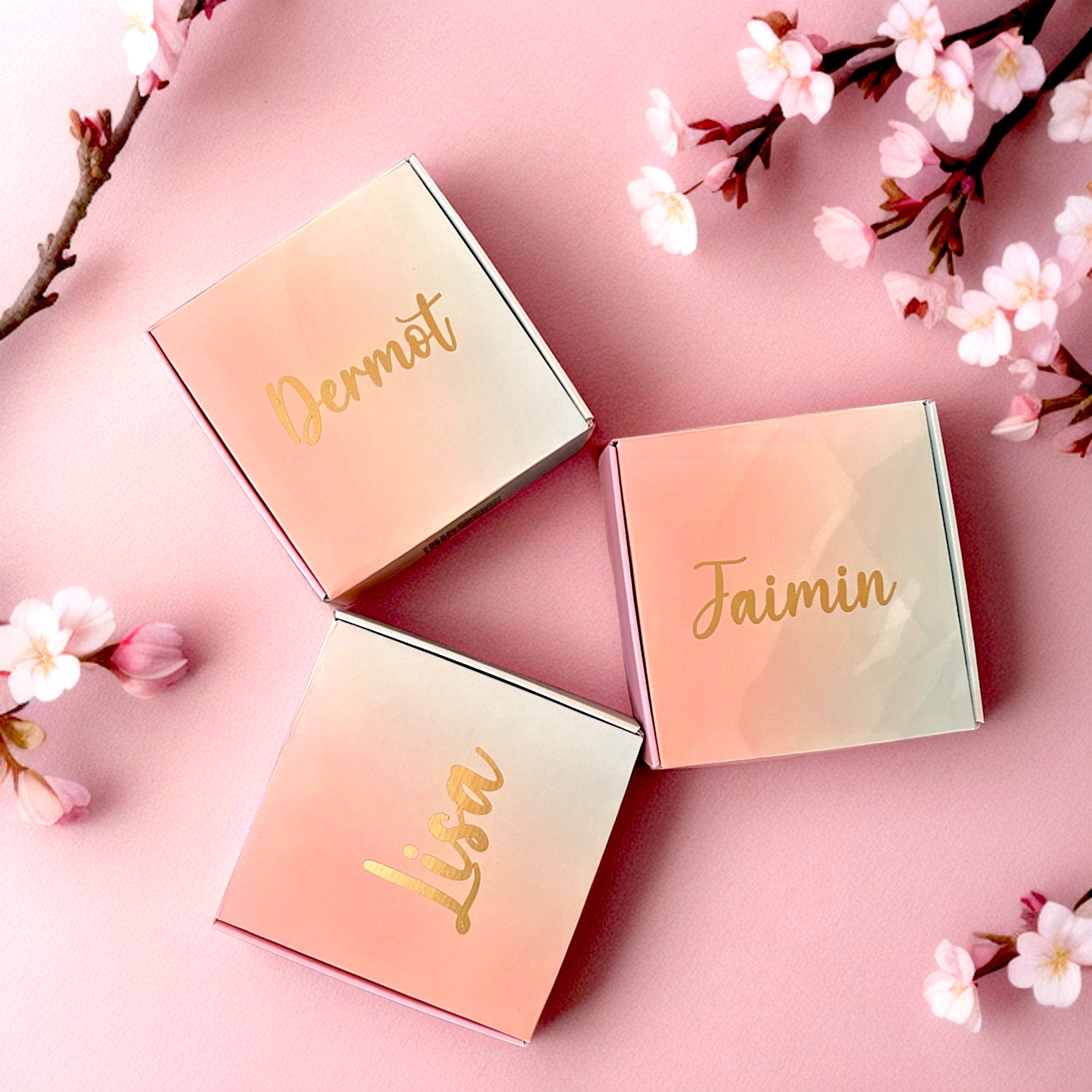 Gift boxes with gradient pink and white colors, gold lettering, and floral arrangement decoration