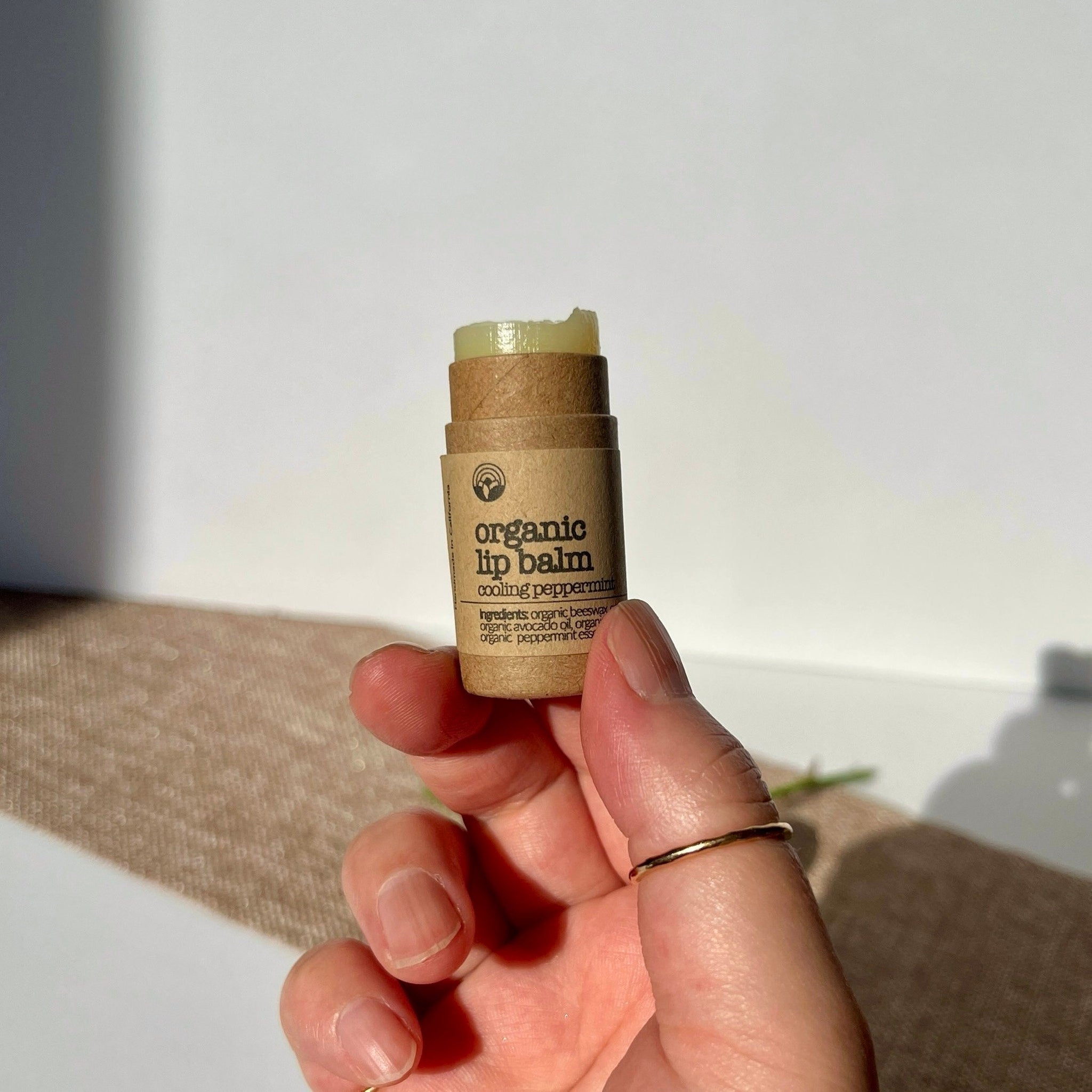 Organic lip balm in brown paper tube with green balm, held in hand near white background