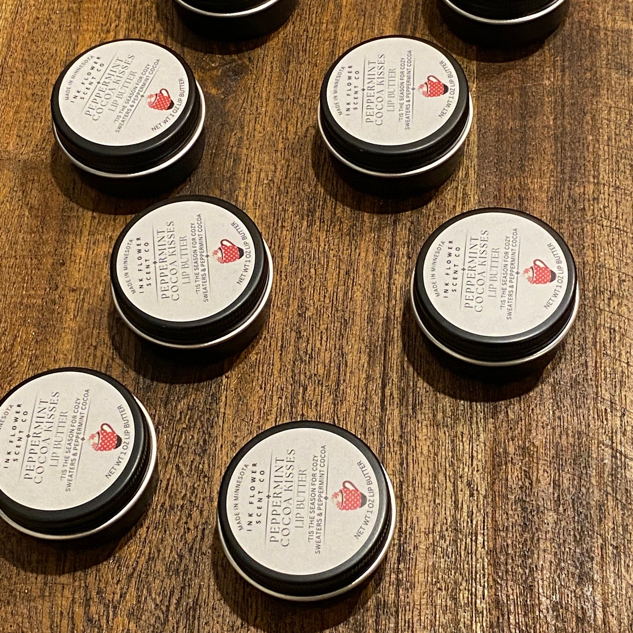 Lip butter tins with black rim, white label, and Ink Flower Scent Co text on wood surface