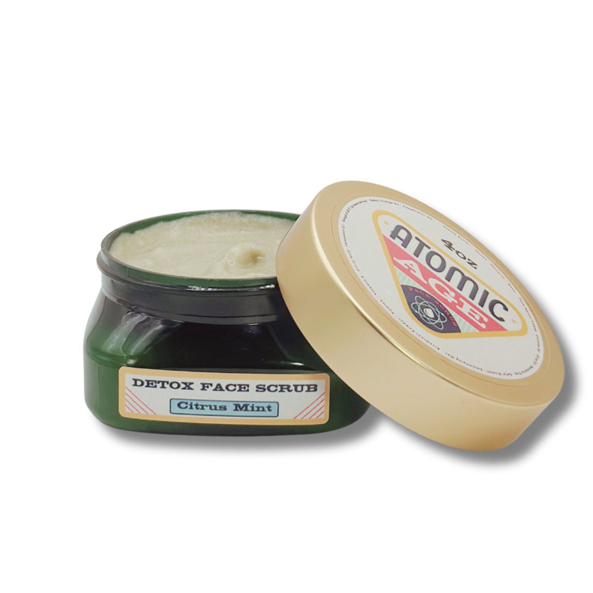 Detox face scrub jar with green glass, gold lid, and white cream contents, Atomic Age brand