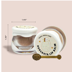 Lip balm in clear glass jar with white lid, brown contents, and gold stirrer