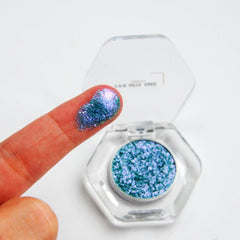 Side view of teal, blue, and silver multichrome eyeshadow pan catching light to reveal iridescent shift