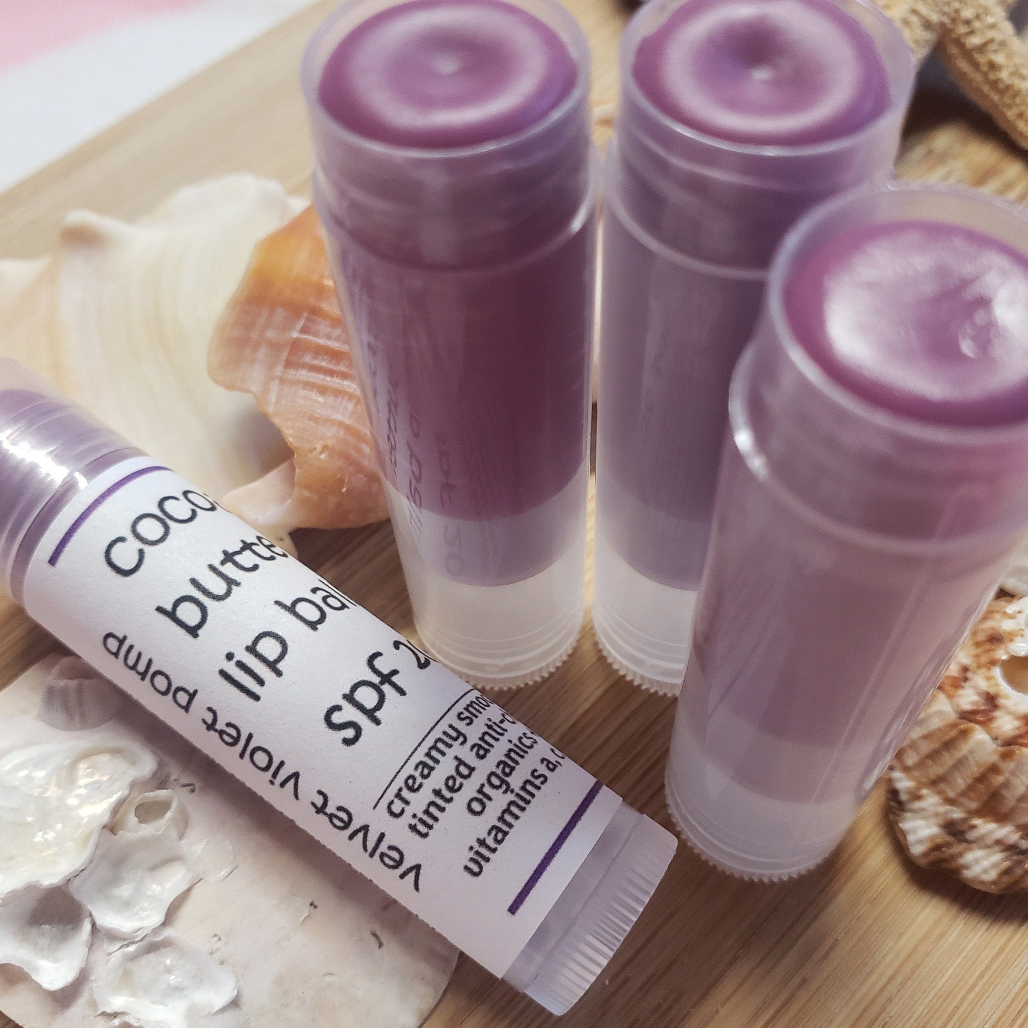 Lip balm sticks with purple tint, clear plastic tube, and white label on wooden surface