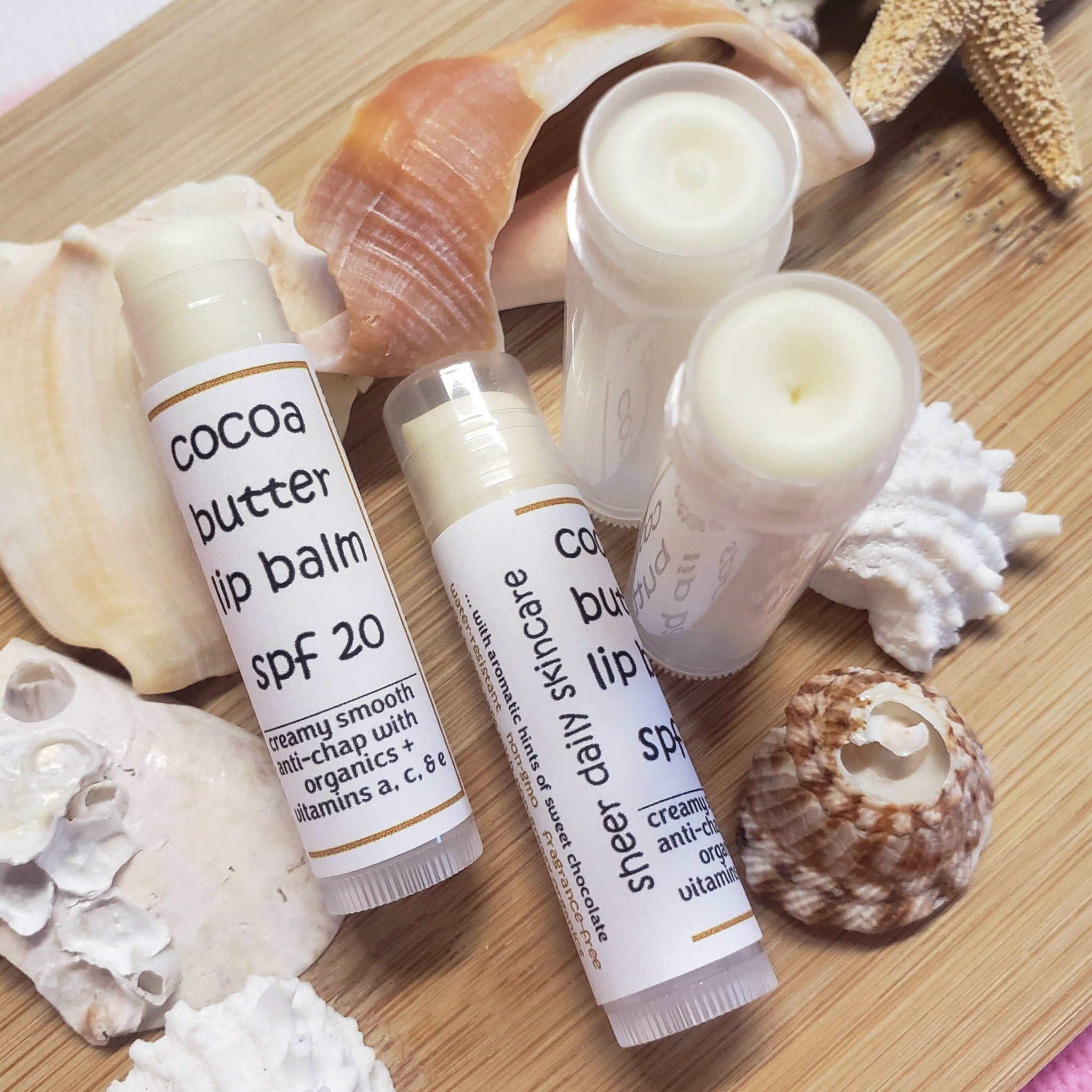 Lip balm tubes with white labels, light beige balm, and clear caps on wooden surface with shells