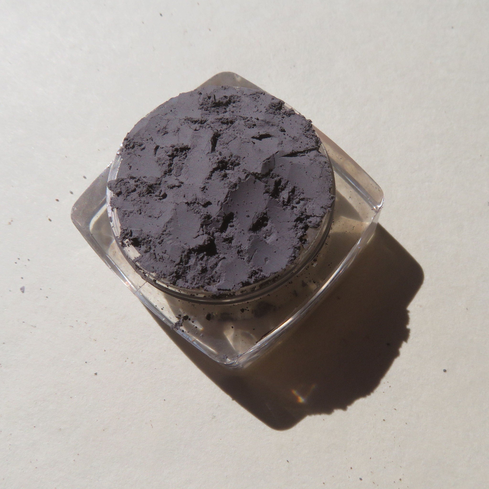 Side view of matte medium gray mica mineral eyeshadow in loose powder form with vegan label visible