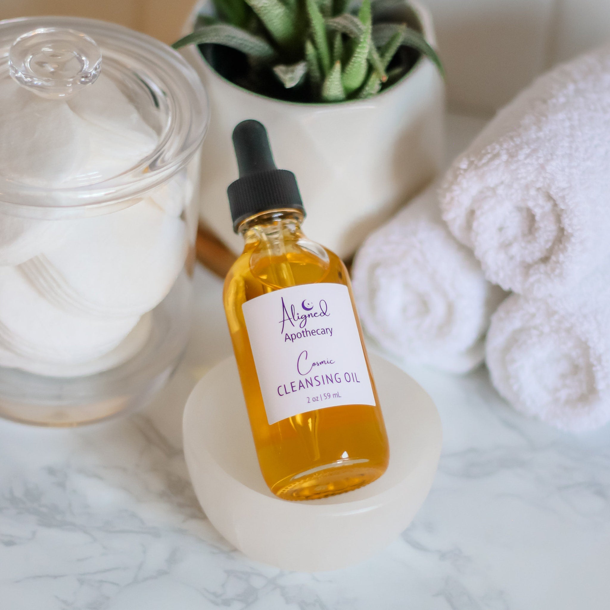 Cosmic cleansing oil bottle with yellow liquid, black dropper, and white label in a bowl on marble surface