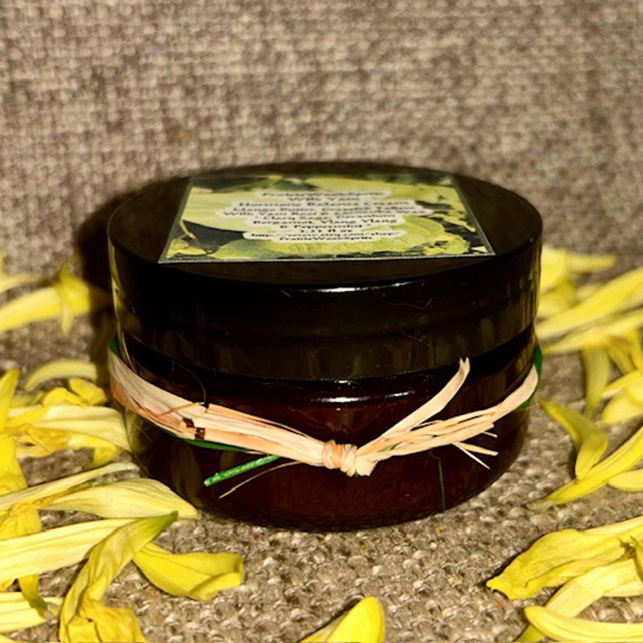 Jar of cream with dark brown glass, raffia tie, and yellow flower petals around it