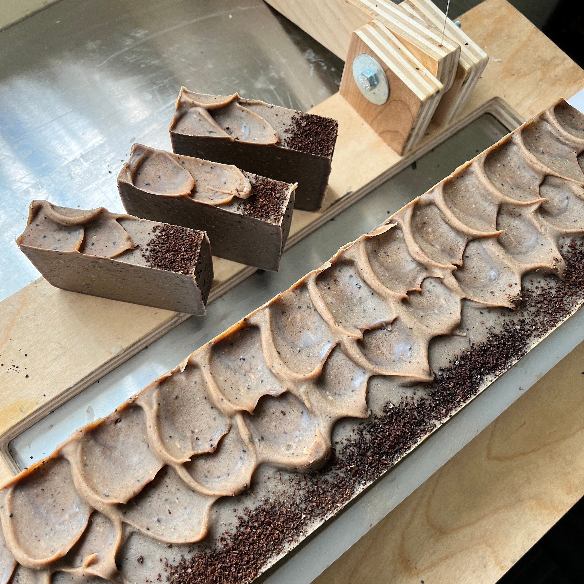 Soap bars with brown and tan colors, textured surface, and small brown granules on a wooden surface