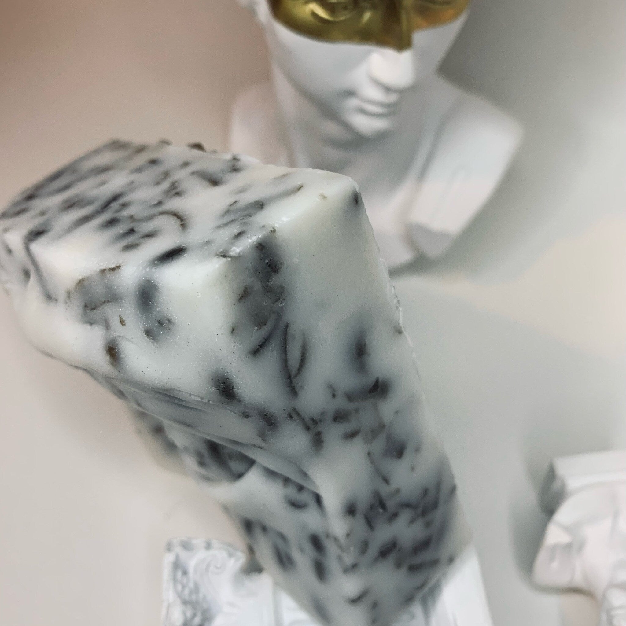 Soap bar with white and black speckled pattern, textured appearance, near white bust statue