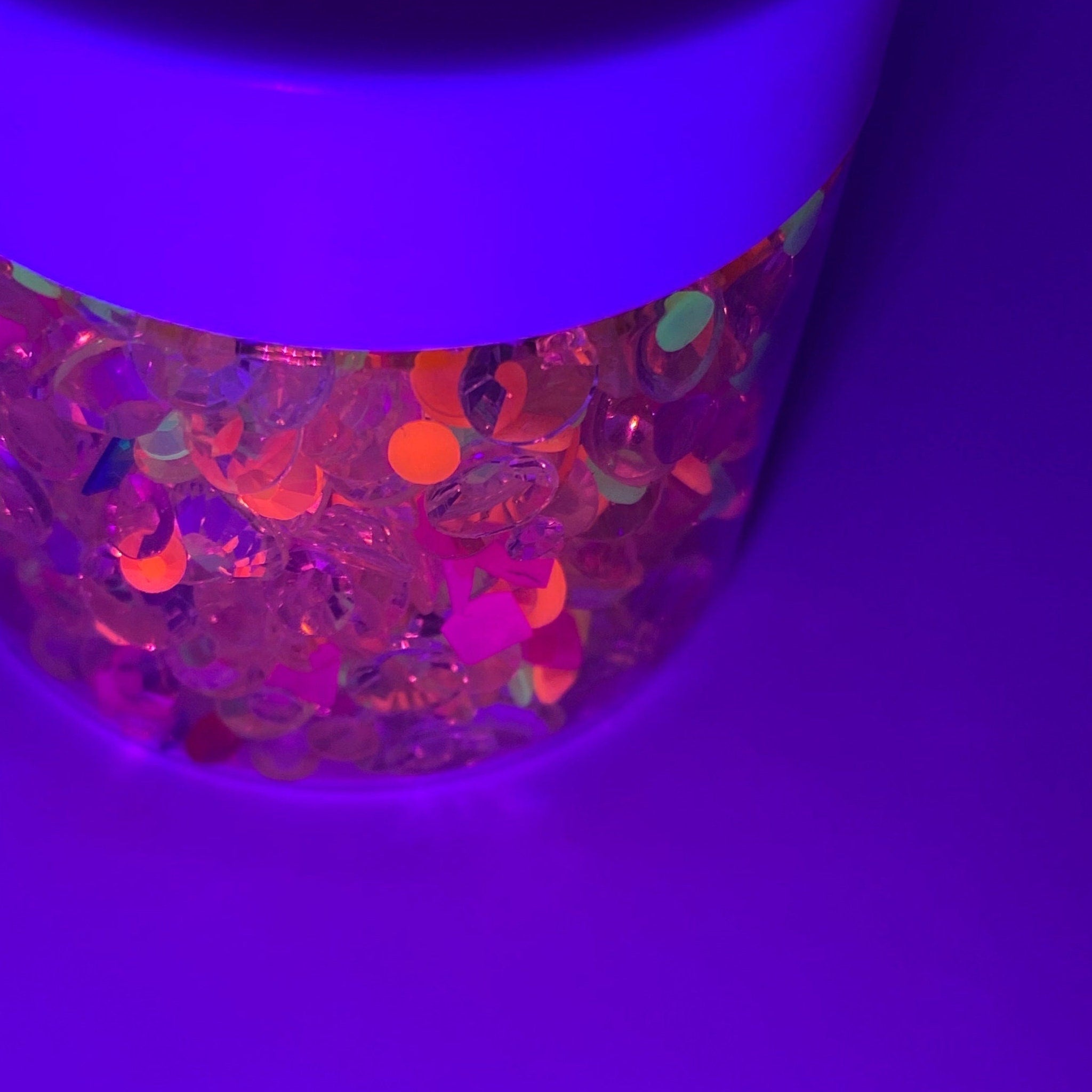 Colorful sequins in clear container, purple and orange tones, iridescent shapes