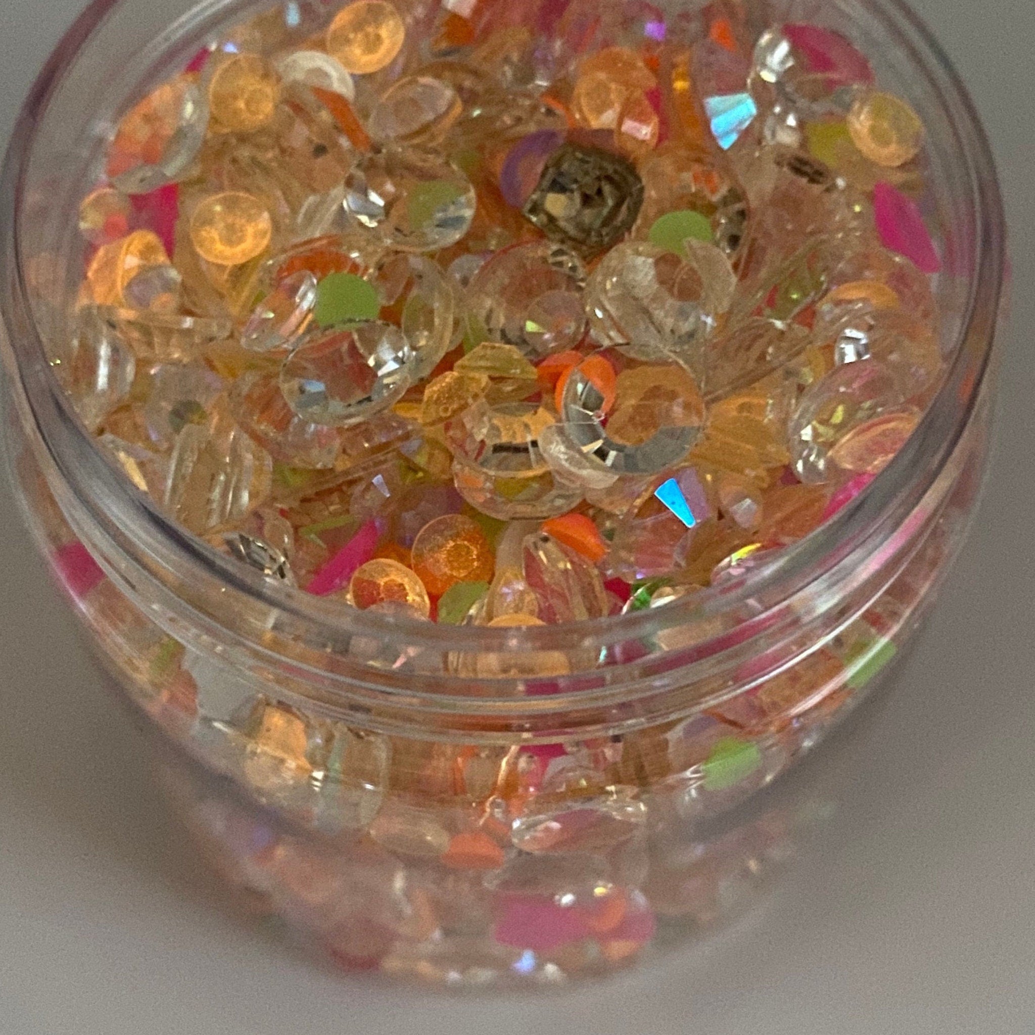 Decorative craft beads in clear, orange, pink, and green colors, inside a clear container