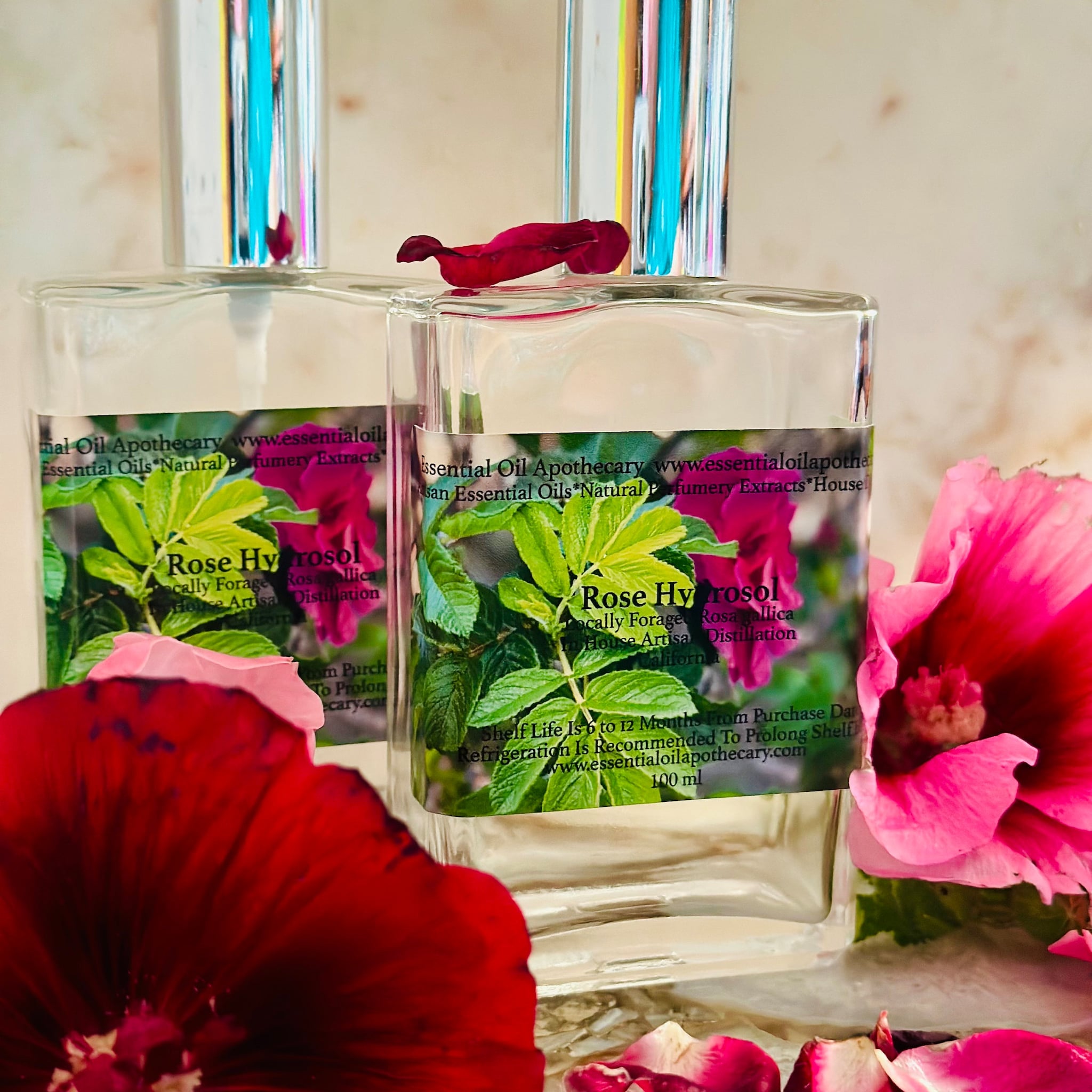 Rose hydrosol bottles with clear glass, silver cap, and red flower petals around them