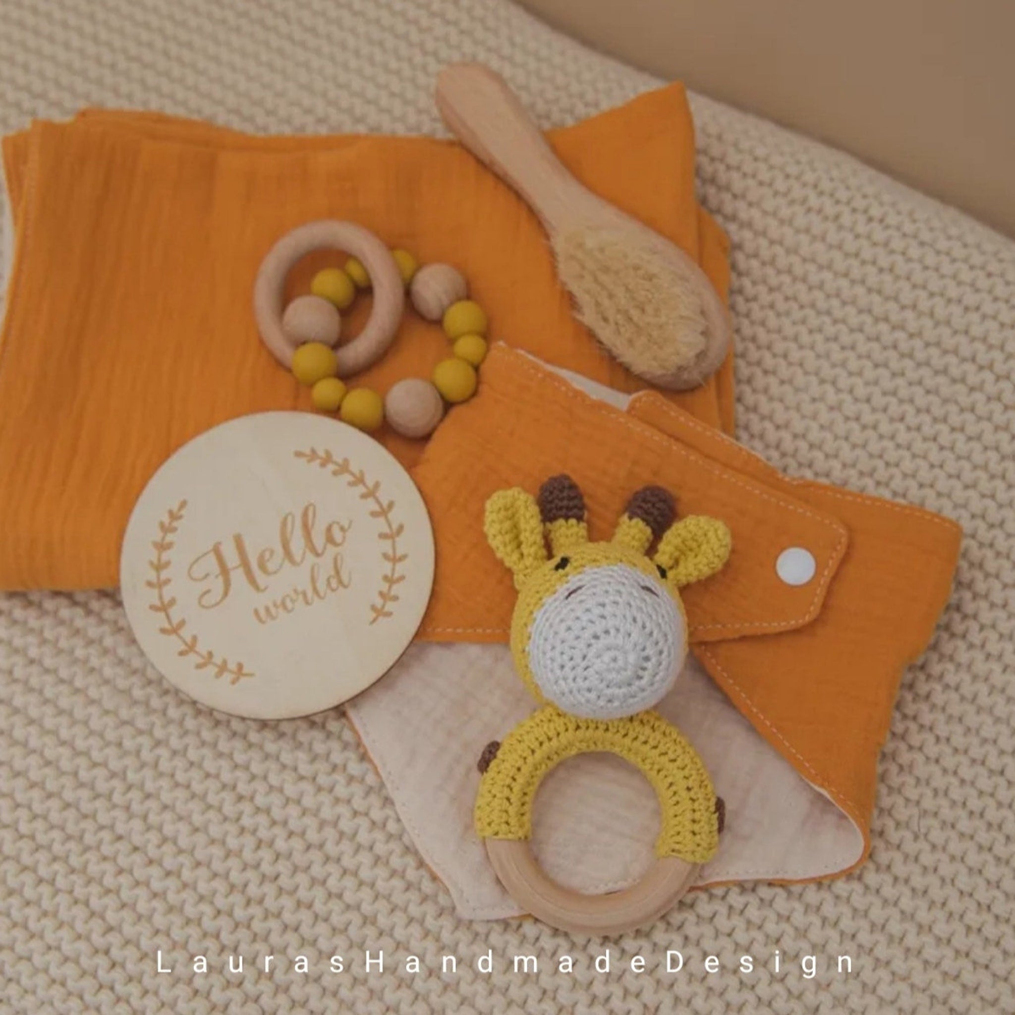 Baby gift set with yellow muslin, wooden teether, and crocheted giraffe rattle on blanket