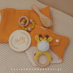 Baby gift set with yellow muslin, wooden teether, and crocheted giraffe rattle on blanket