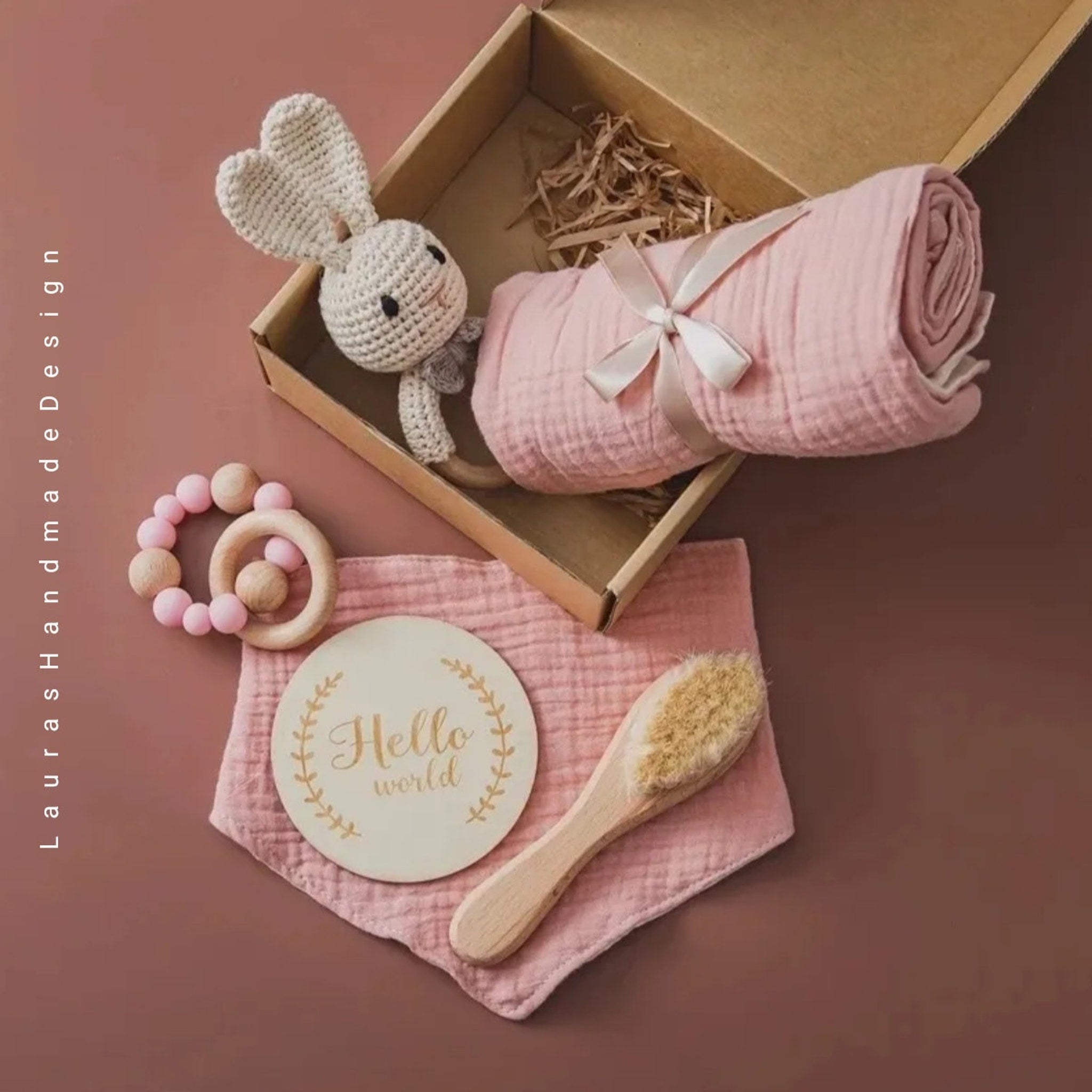 Baby gift set with pink muslin blanket, crochet bunny, wooden teether, and bib in box