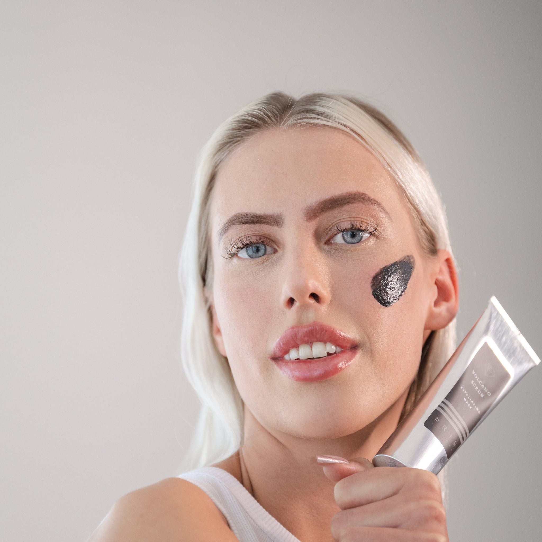 Exfoliating mask with black formula, silver tube, and woman's face with product applied