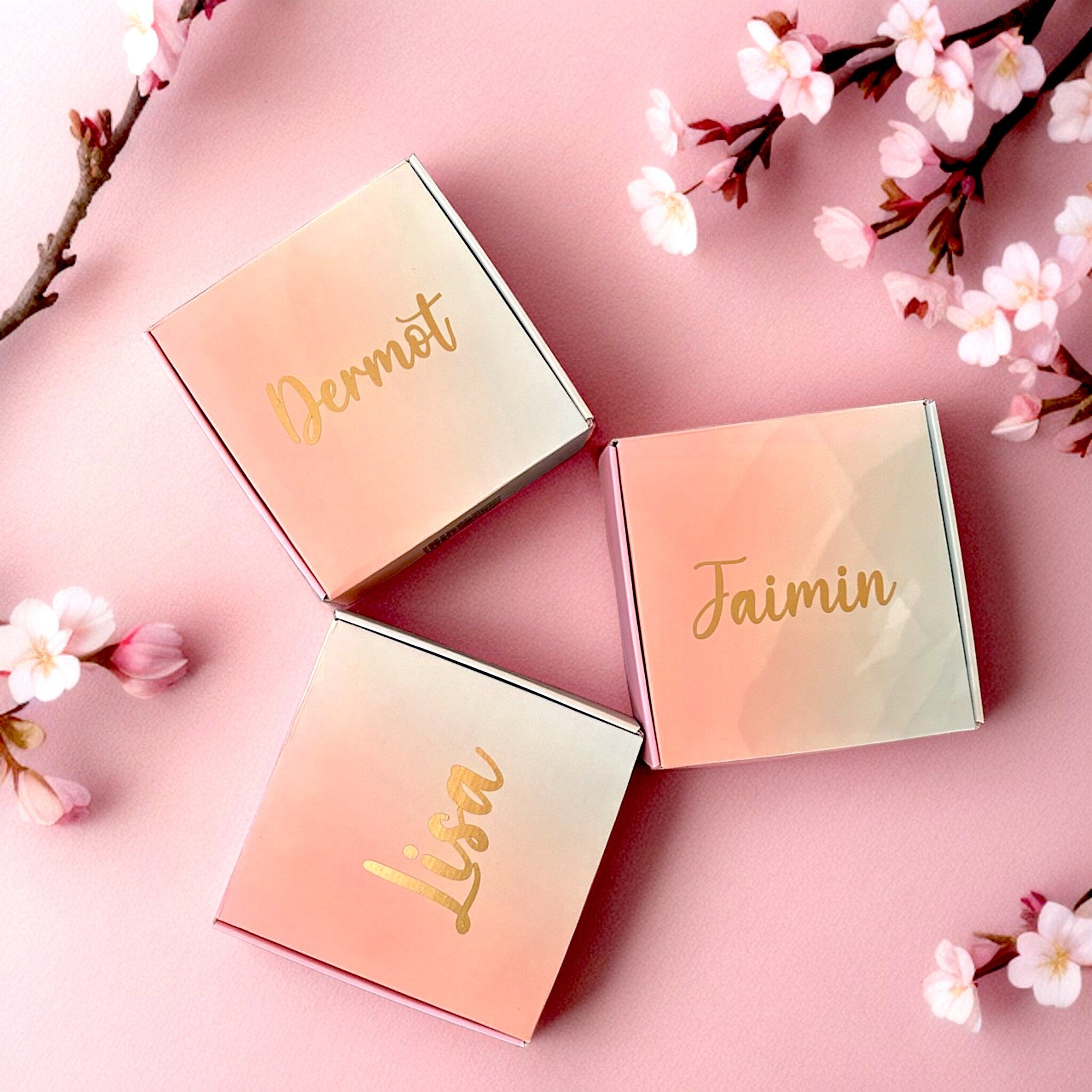 Gift boxes with pink and white gradient, gold lettering, and floral arrangement