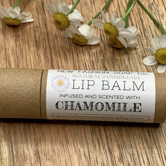 Lip balm tube with white label, brown paper, and chamomile flowers on wood surface.