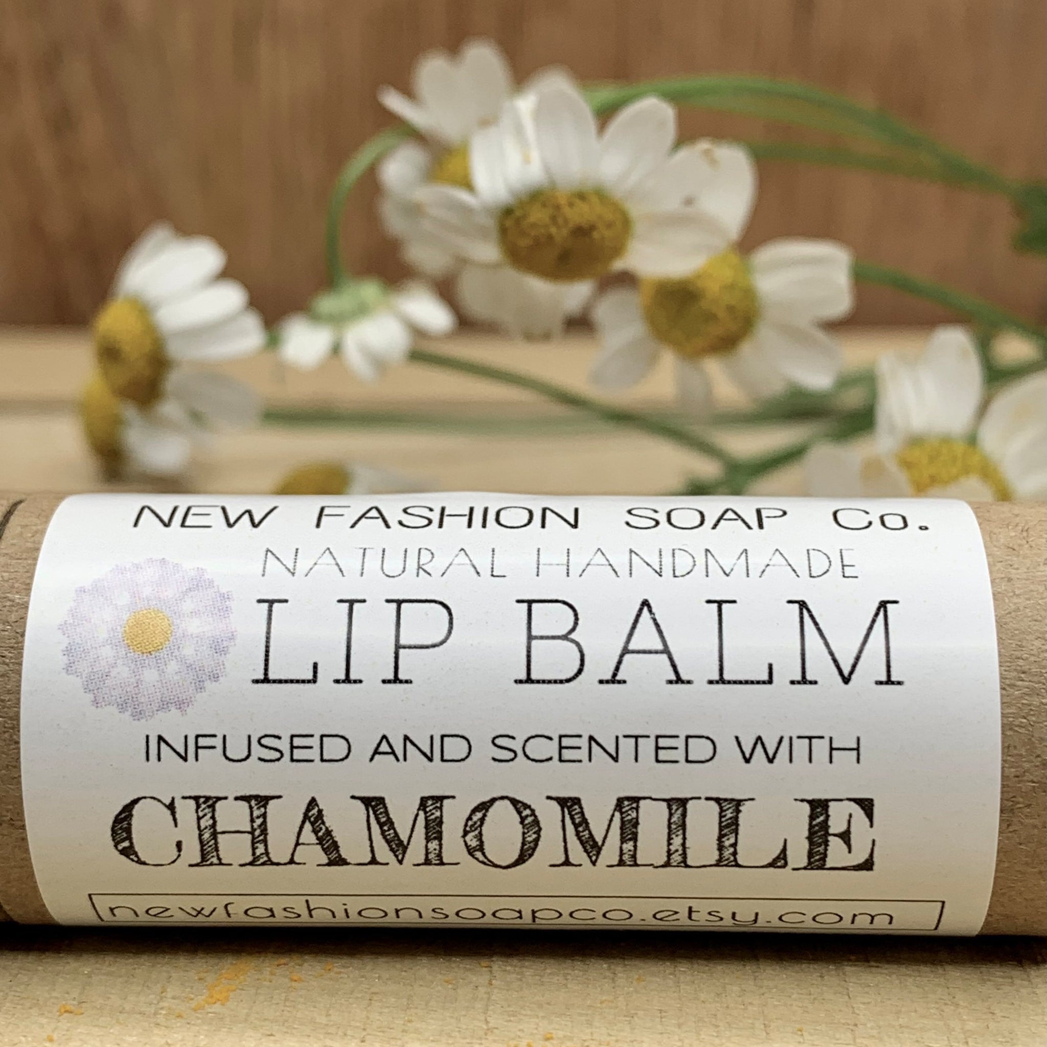 Lip balm tube with white label, brown paper, and chamomile flowers in background