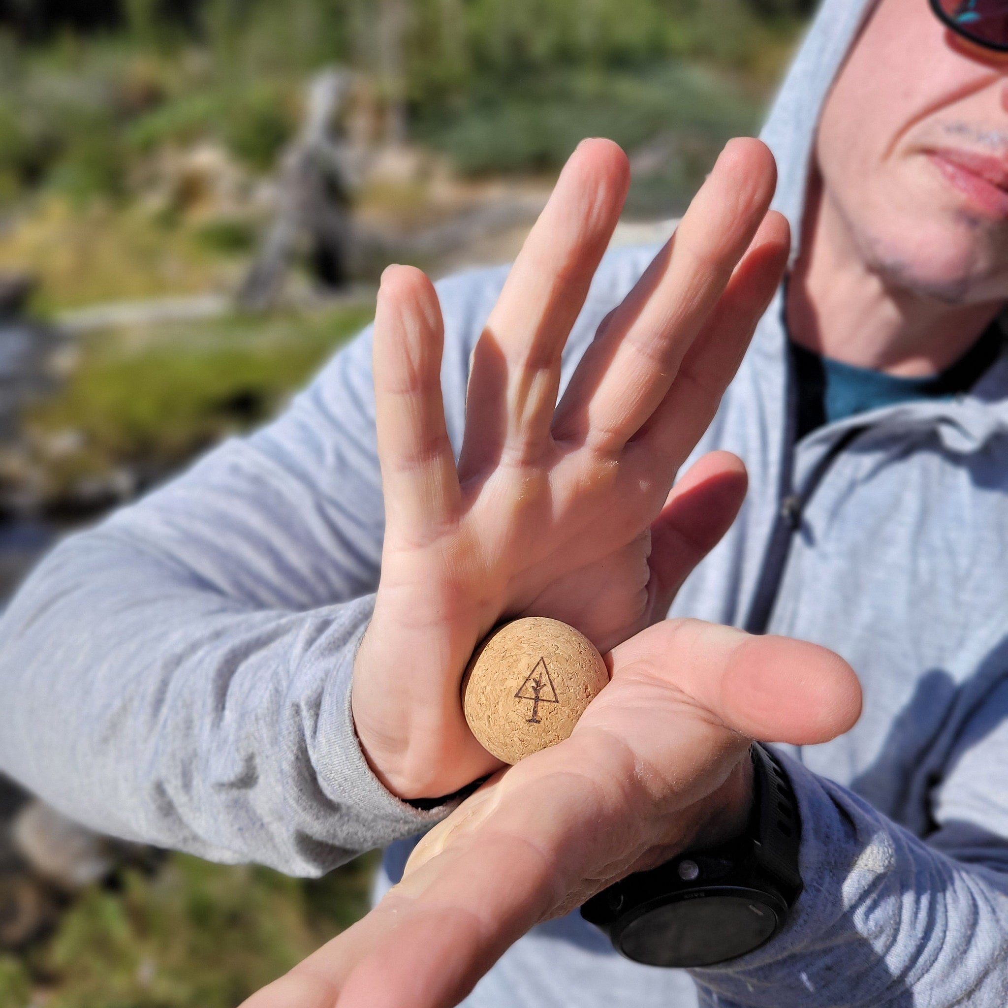 Cork ball with tree logo, held in hands, with gray hoodie and watch visible