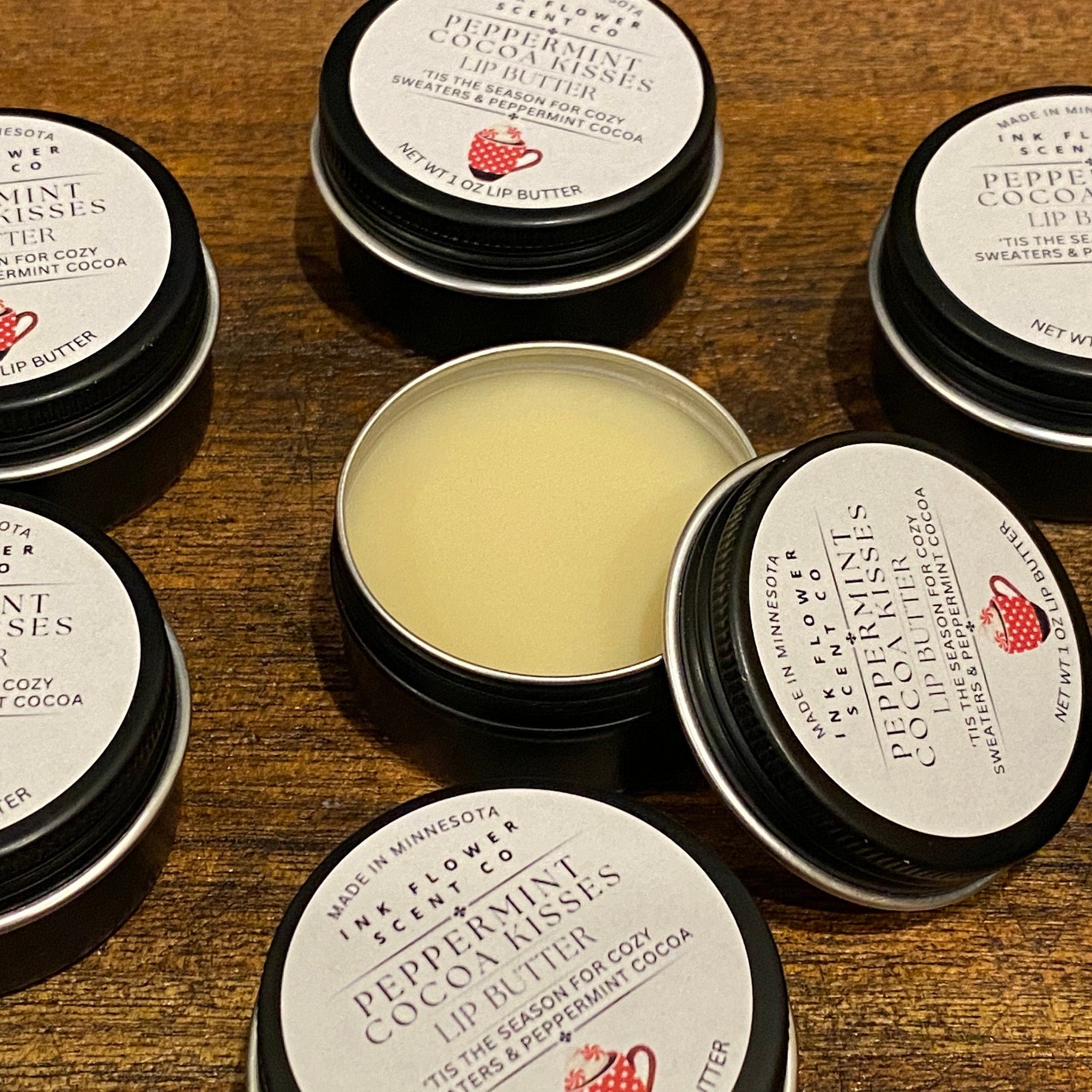 Lip butter tins with black lids and white labels, Ink Flower Scent Co brand, on wood surface