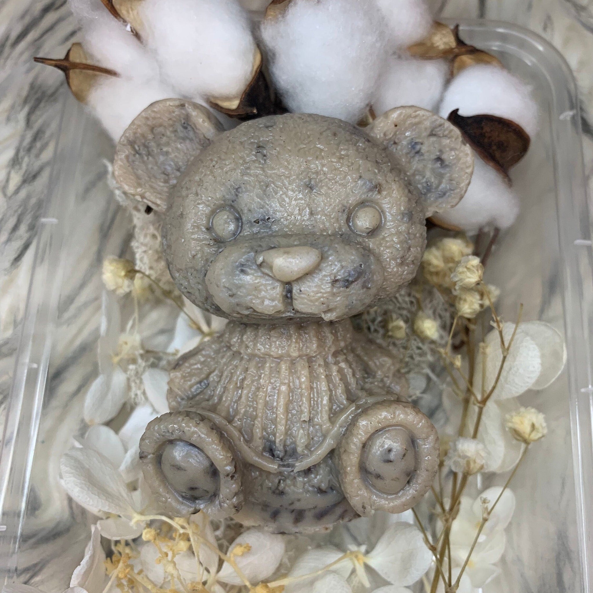 Teddy bear soap in gray with visible texture, surrounded by white flowers and cotton