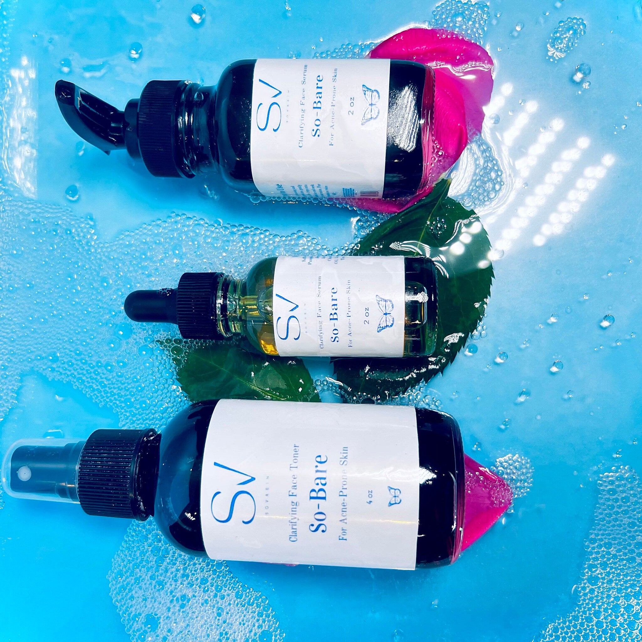 Clarifying face serum bottles, black glass, white labels, "So-Bare" text, in water with bubbles and flower petals