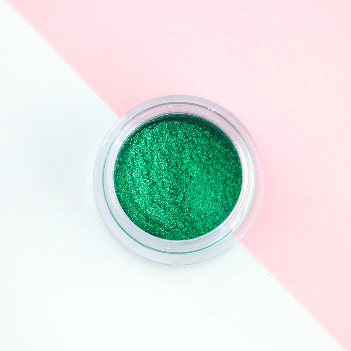 Dark green metallic loose eyeshadow pigment with intense shimmer in a small jar, perfect for festive makeup looks.