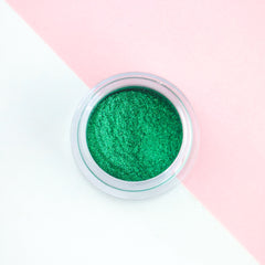 Dark green metallic loose eyeshadow pigment with intense shimmer in a small jar, perfect for festive makeup looks.