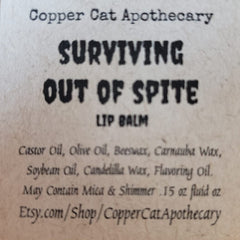 Lip balm label with black text on off-white paper, "Surviving Out of Spite" text, Copper Cat Apothecary brand