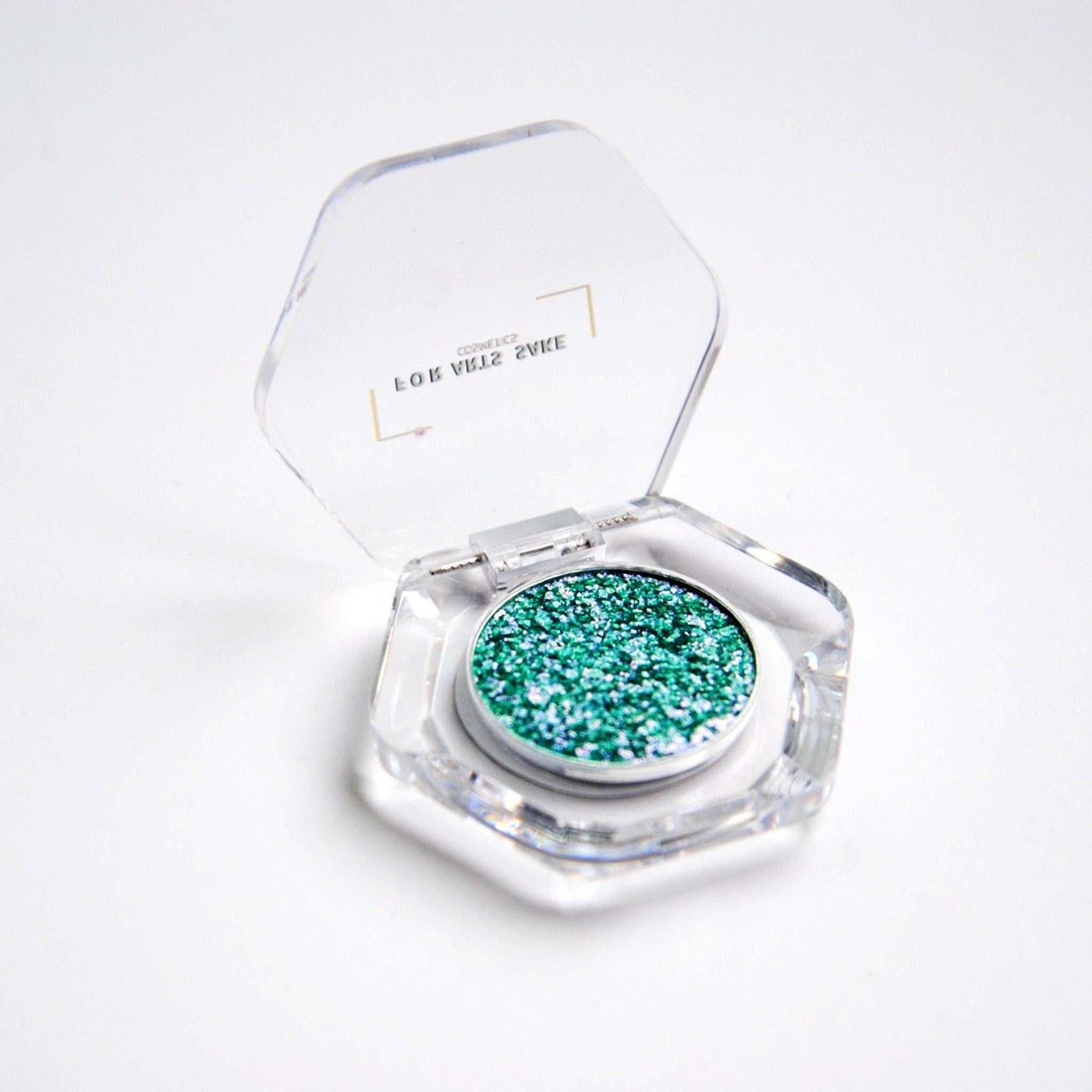 Single eyeshadow pan with teal, blue, and silver iridescent duochrome shift in compact packaging
