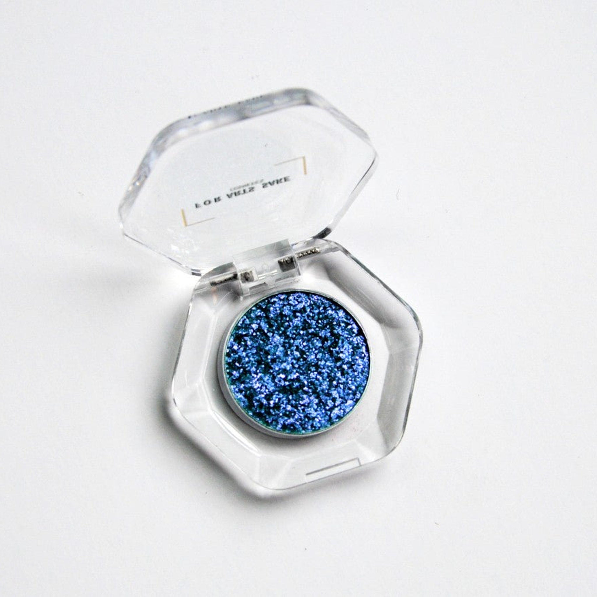 Square compact with teal, blue, and silver multichrome eyeshadow in matte black packaging
