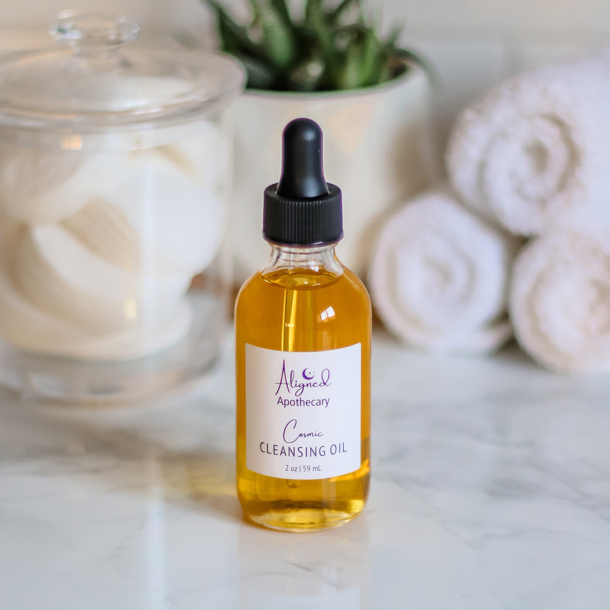 Cleansing oil bottle with yellow liquid, black dropper, and white label with text from Aligned Apothecary
