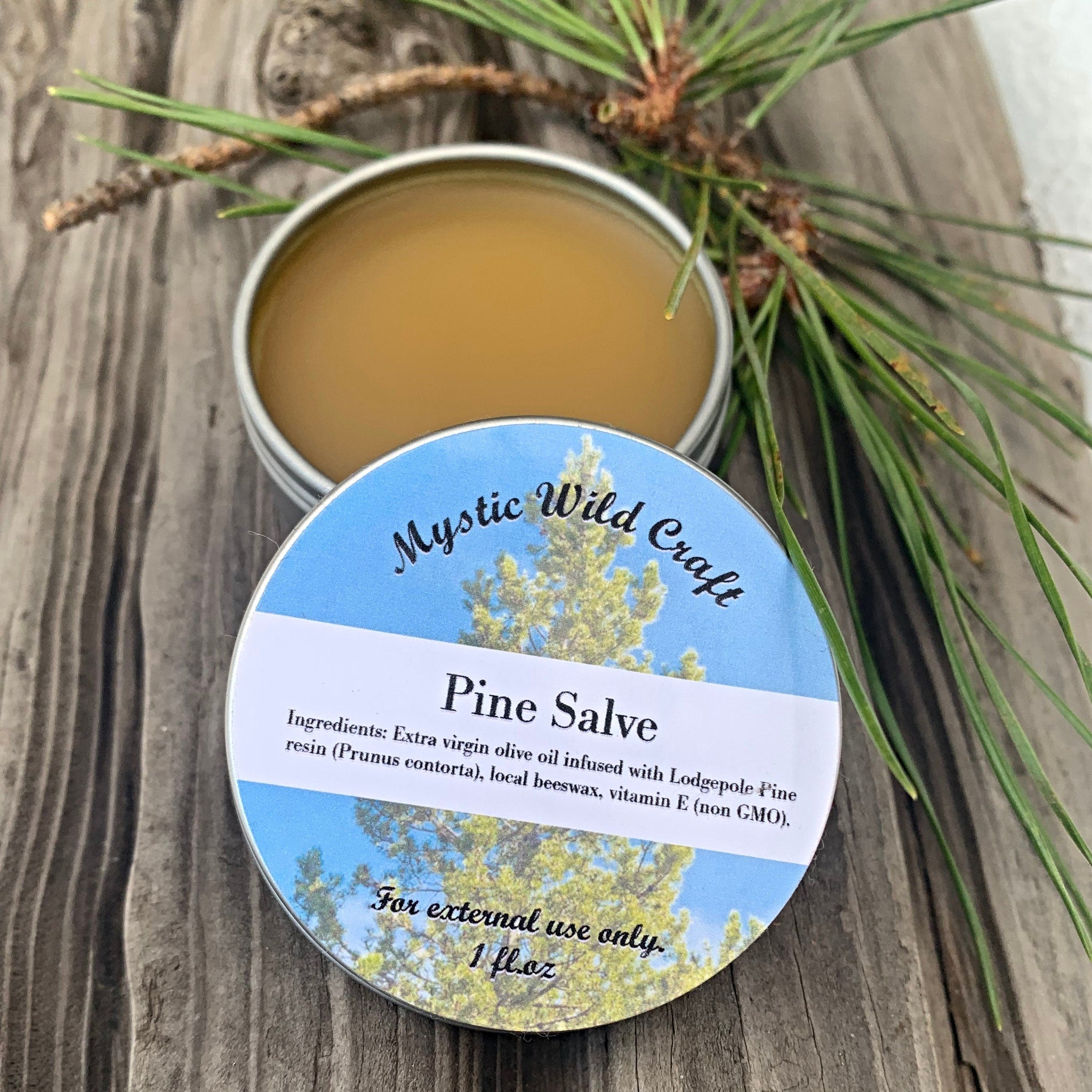 Hand scooping rich amber pine salve from a glass jar onto fingertips in natural light