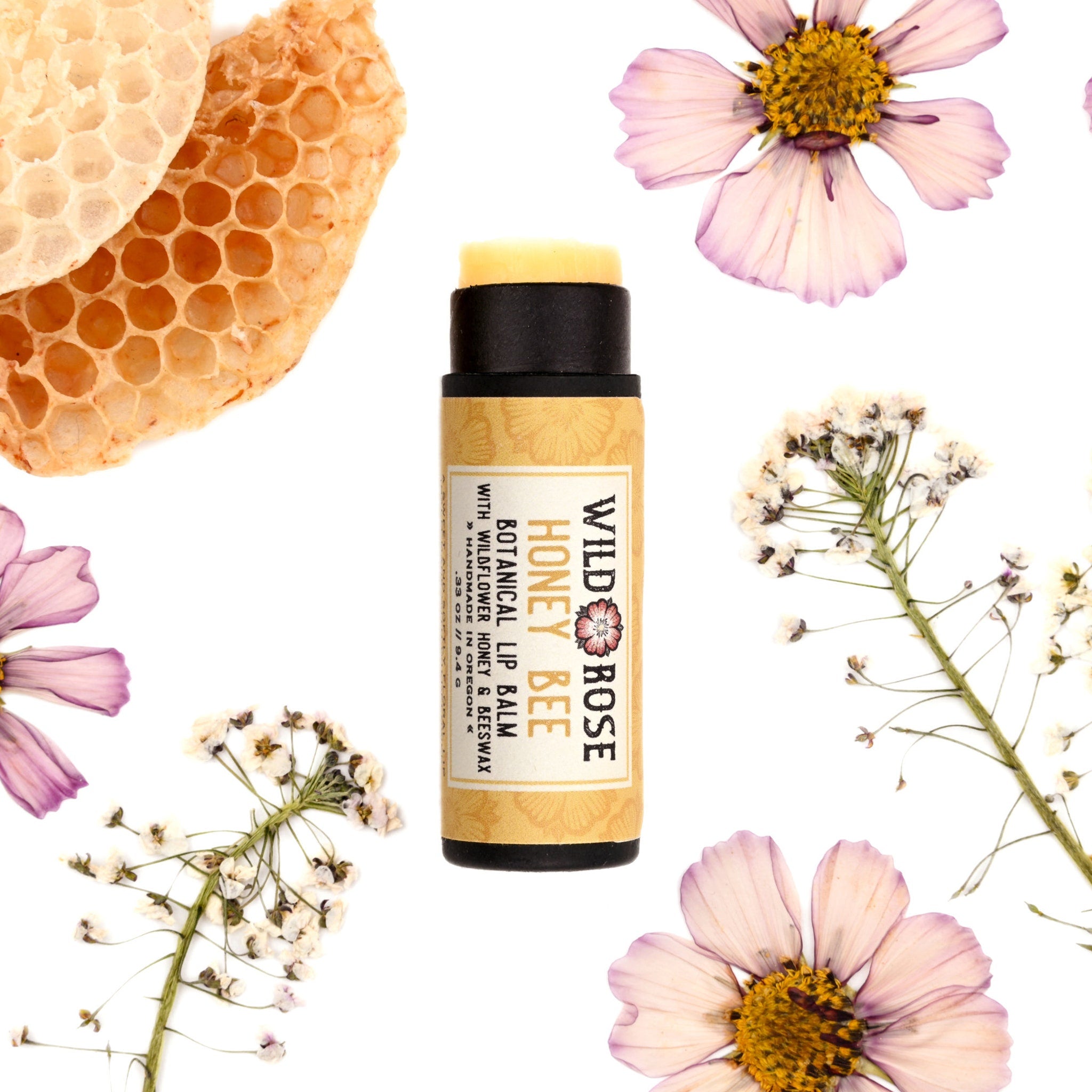 Lip balm tube with black cap and yellow label, surrounded by flowers and honeycomb, Wild Rose brand